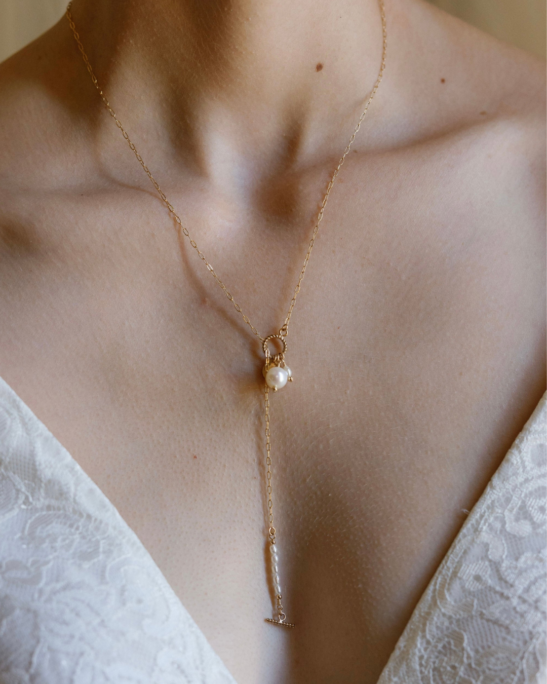 Gold necklace with a pearl pendant on a person wearing a white lace garment wedding dress.