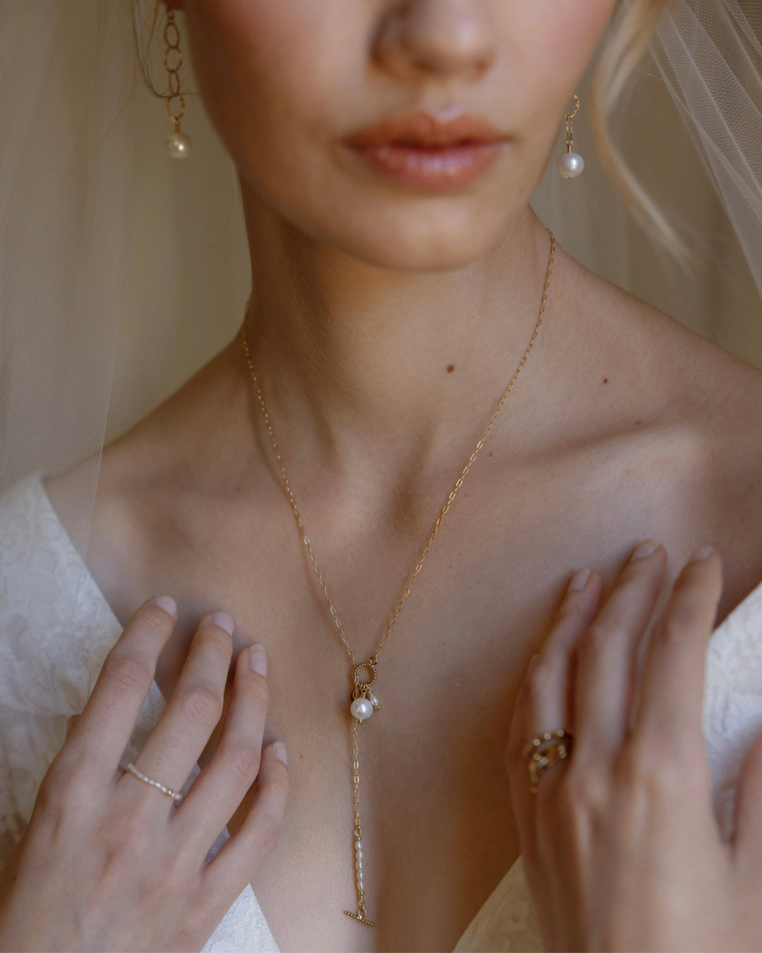 Close-up of a bride wearing a gold necklace with a pearl pendant, earrings, and rings.