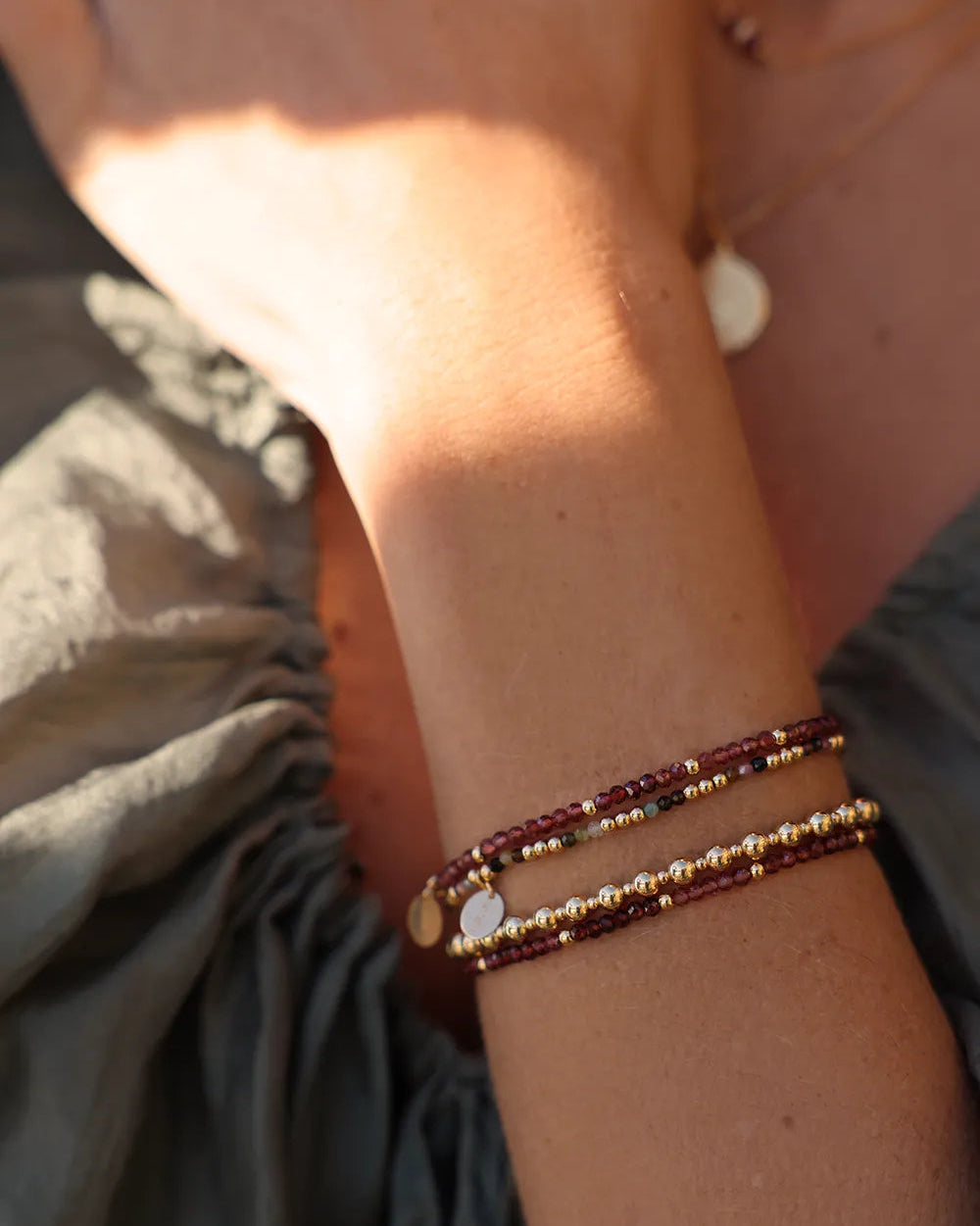 Model wearing beaded bracelet with Gold beads and faceted Garnet gemstones and a gold charm