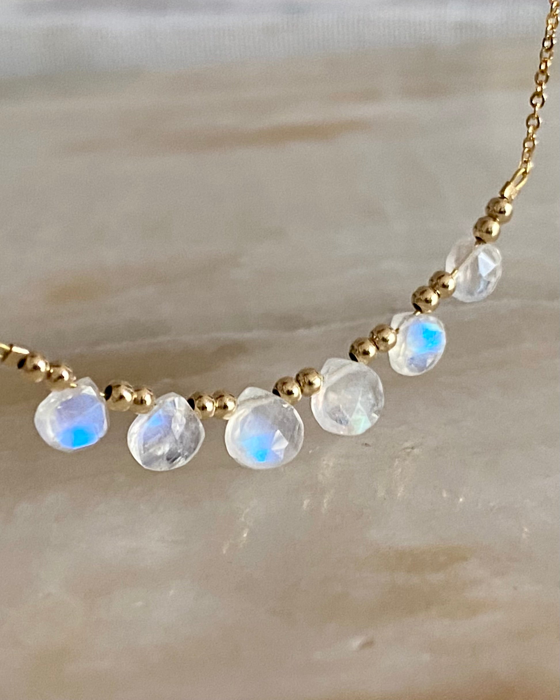 Close up of Necklace with gold chain and faceted moonstone beads on a neutral background