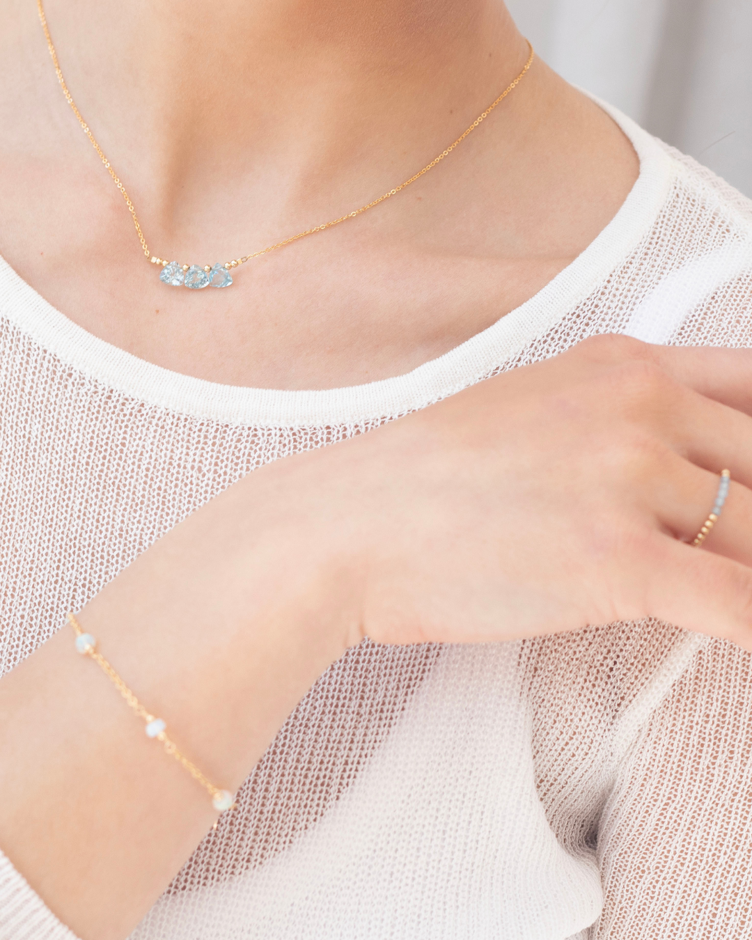 Gold necklace with blue topaz briolette gemstones, bracelet, and a ring and bracelet on a woman wearing a white top.