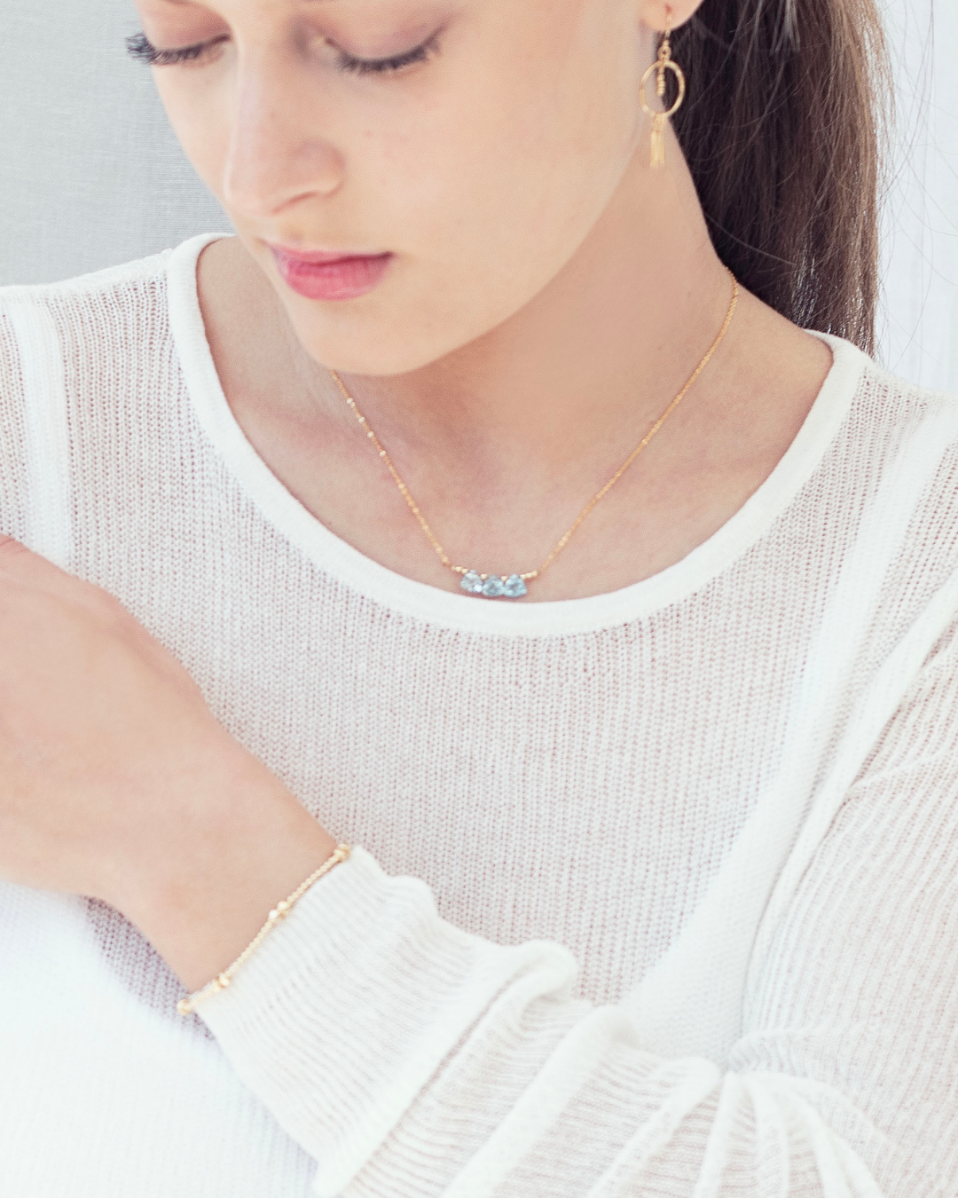 Close up of a woman wearing a delicate gold necklace with blue topaz briolette gemstones, bracelet and earrings.