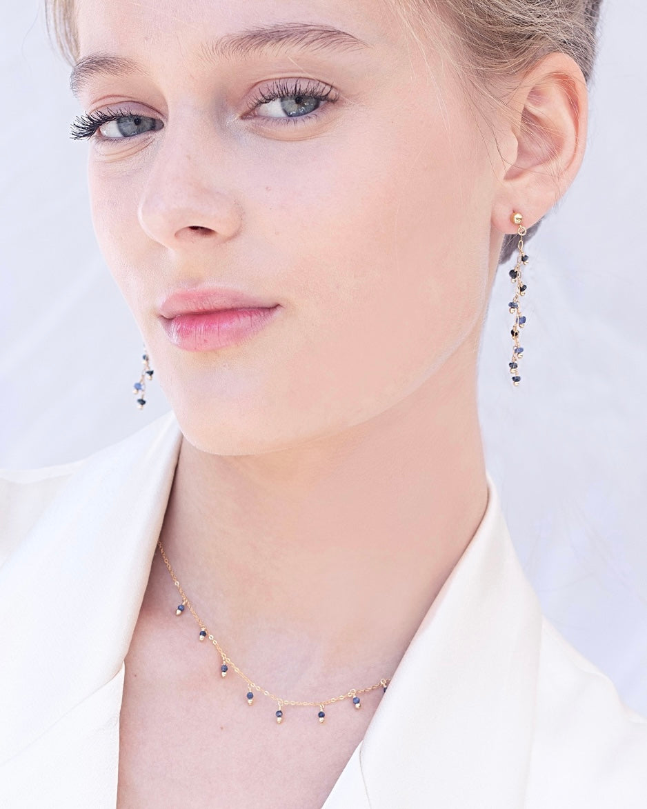 Close-up of a woman wearing blue sapphire earrings and a necklace against a light background