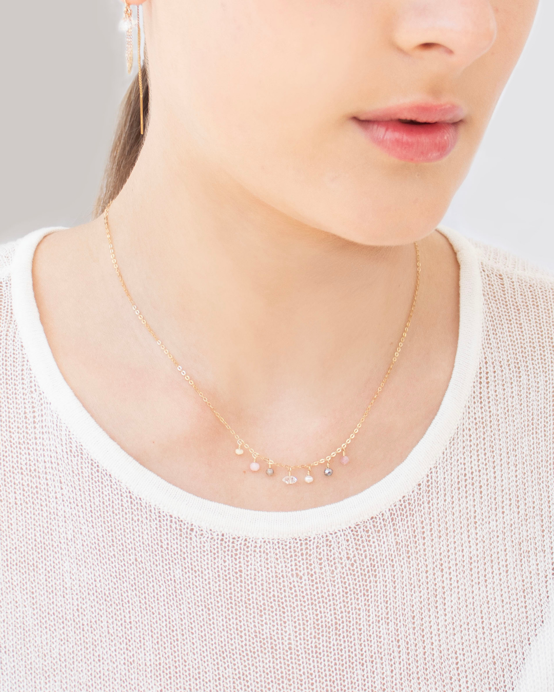 A necklace with small mixed gemstones worn by a woman on a plain background
