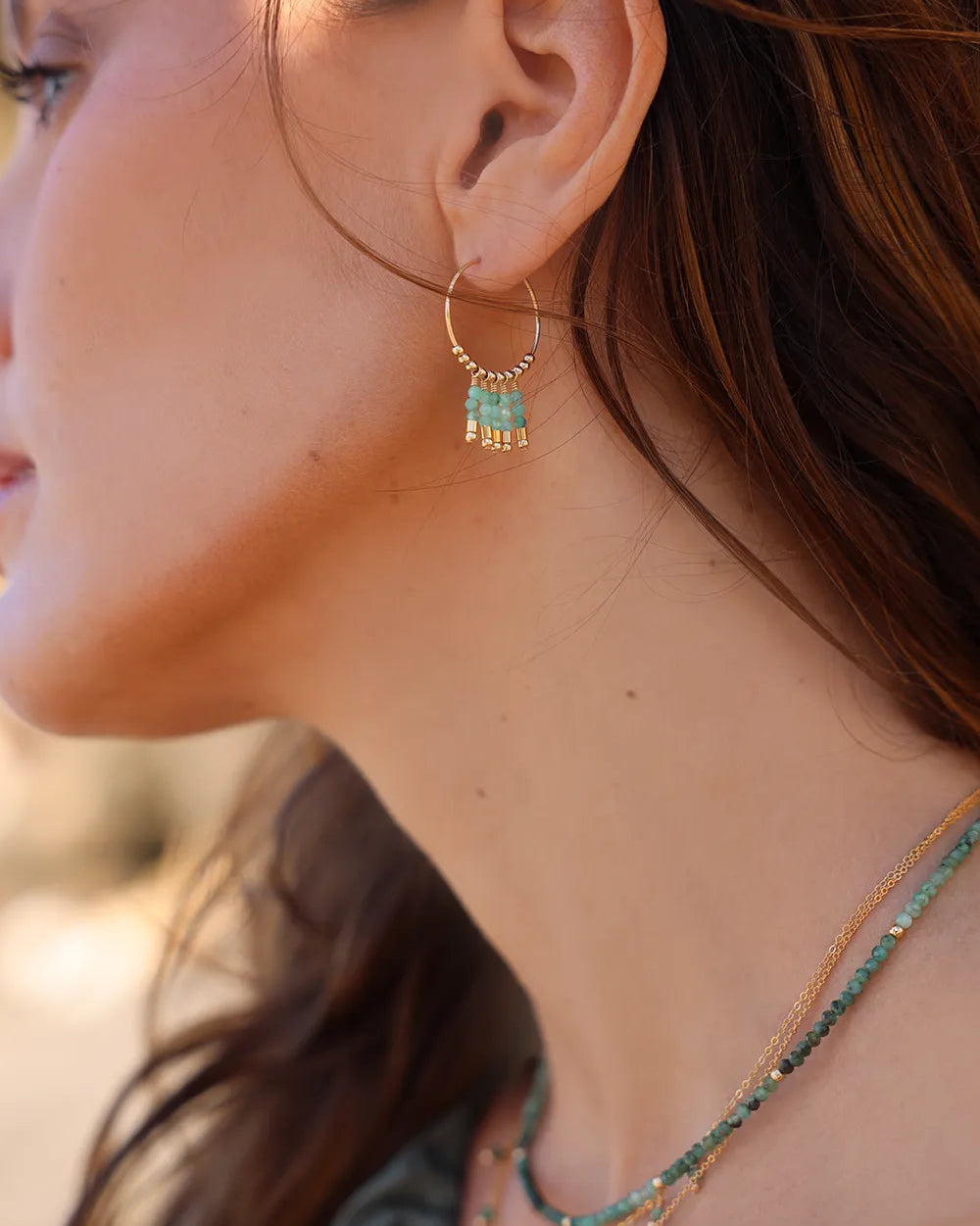Close-up of a woman wearing gold hoop earrings with Emerald gemstones.