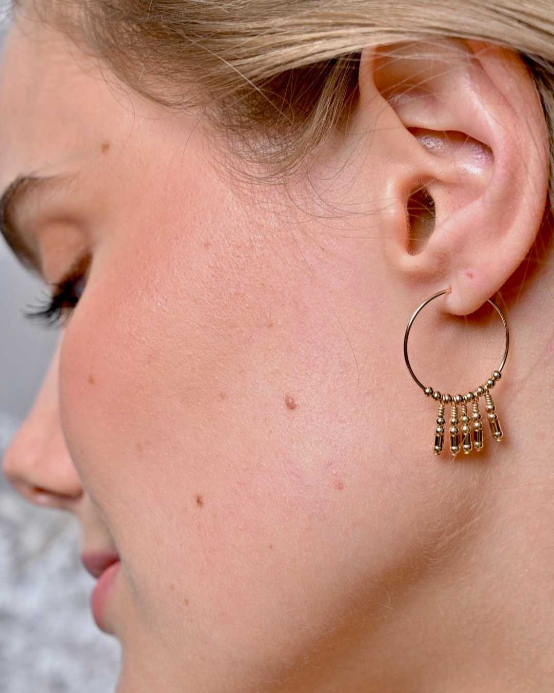 Close-up of a person wearing a gold hoop earring with dangling elements.