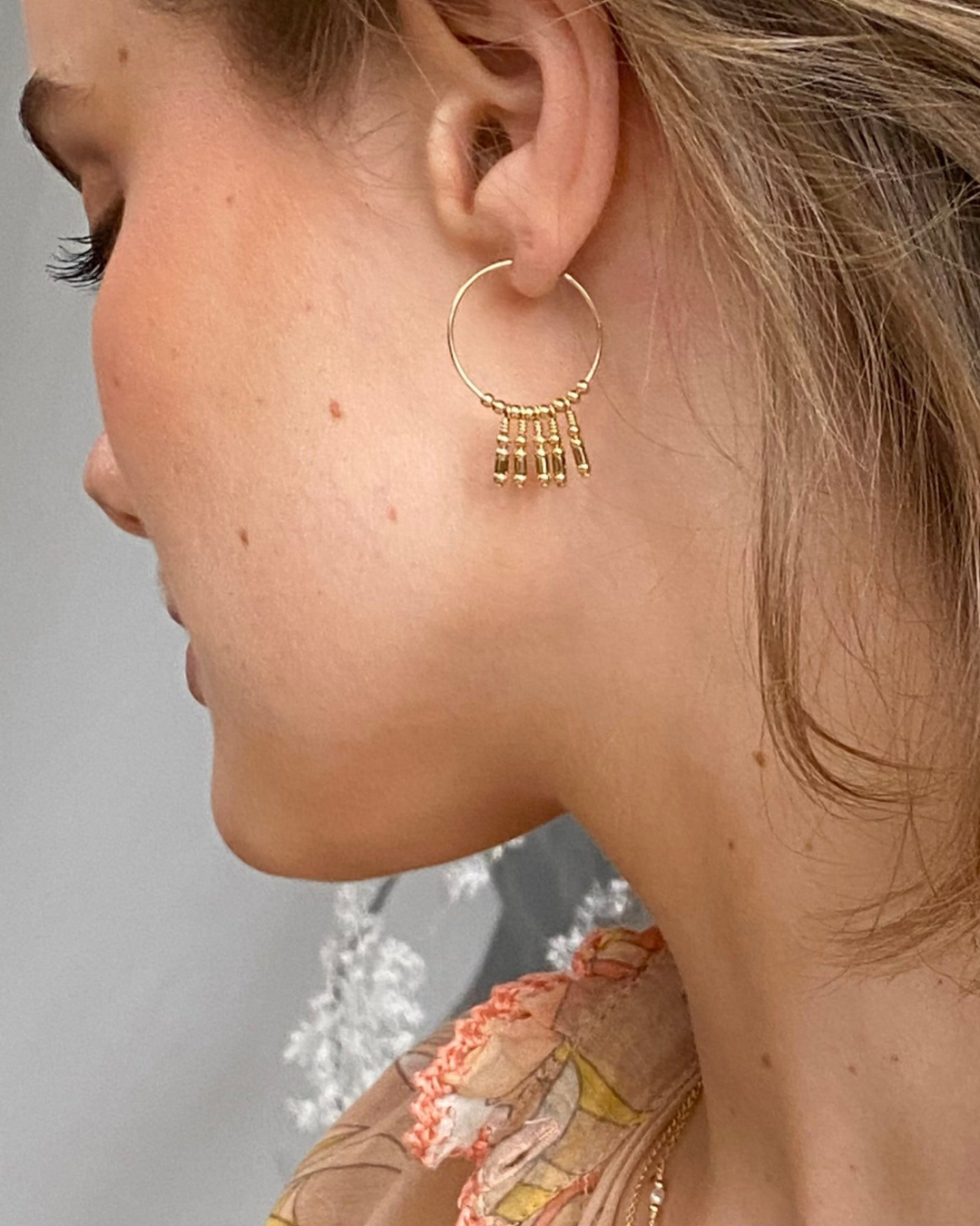 Close-up of a gold hoop earring with dangling elements worn by a person.