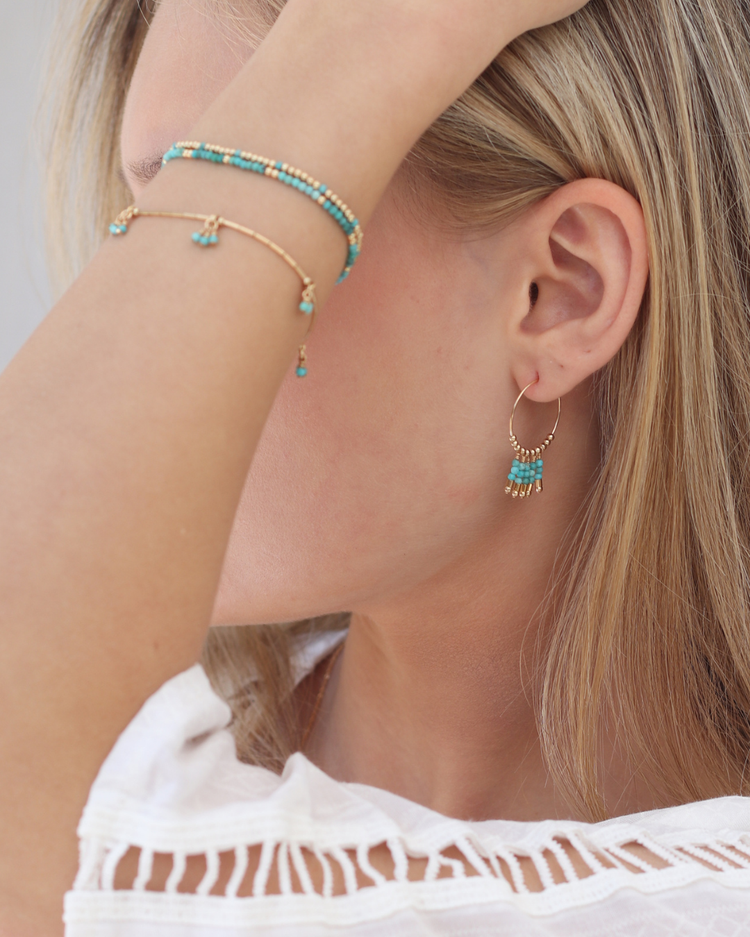 Close-up of a woman wearing gold hoop earrings with turquoise gemstones and matching bracelets.