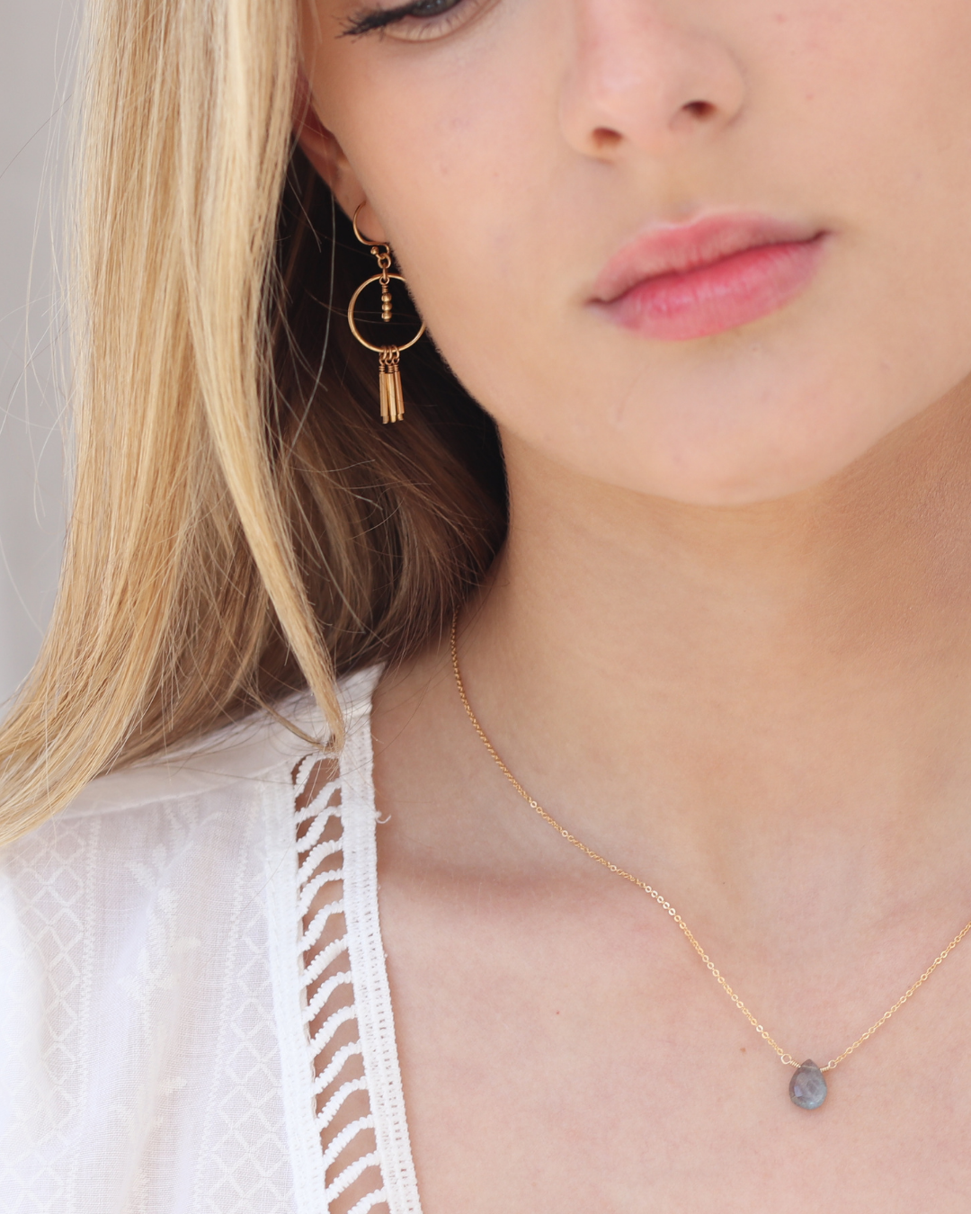 Close-up of a woman wearing gold earrings and a labradorite necklace with a white top.