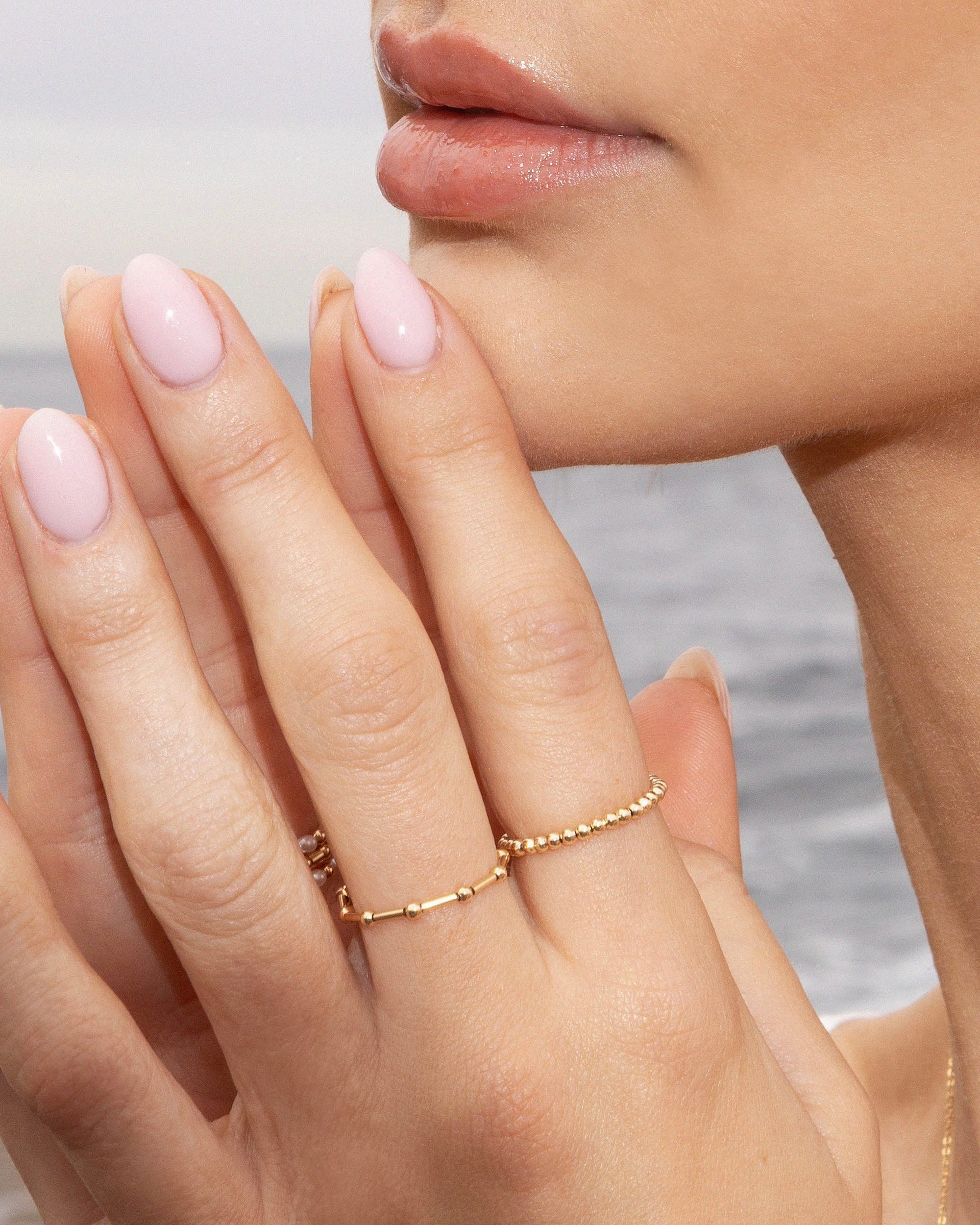 Close-up of a woman's hand with pink nail polish and a gold ring, against a blurred natural background.