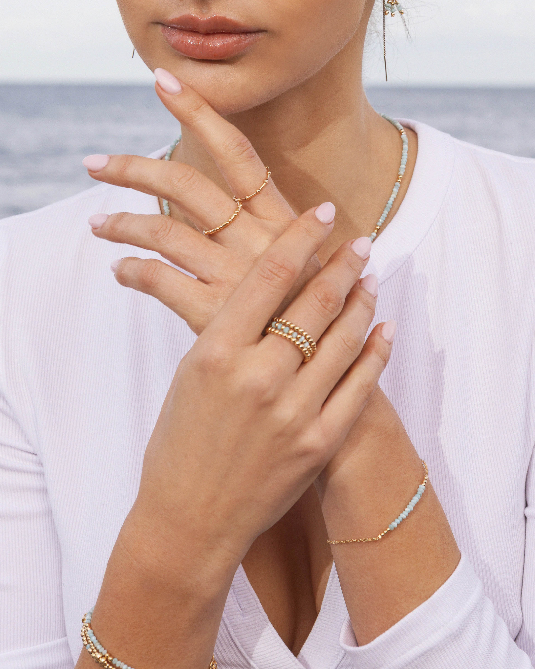 Close-up of a person's hand wearing multiple gold rings and bracelets against a blurred natural background