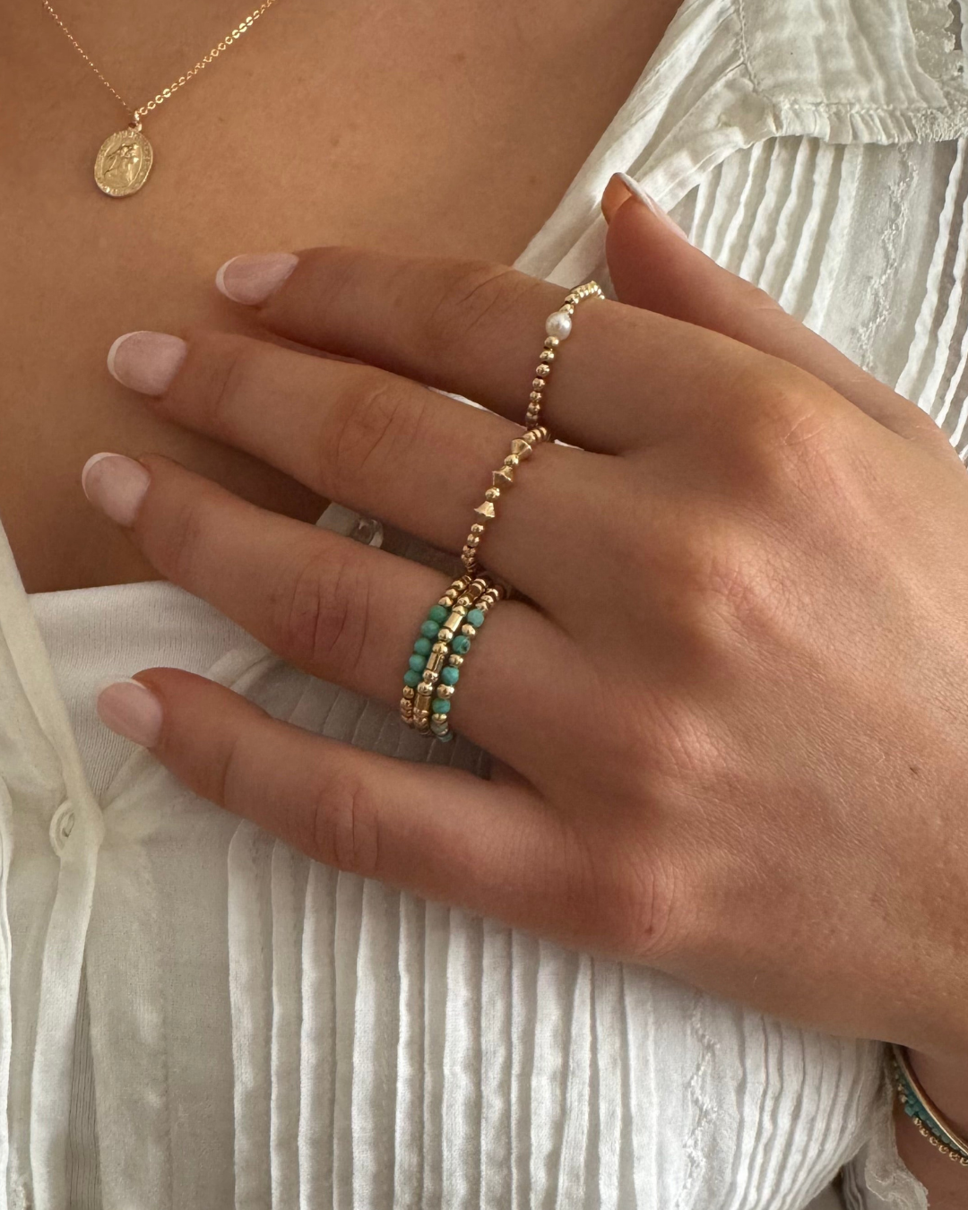 Close-up of a hand wearing gold rings with turquoise stones on a white background