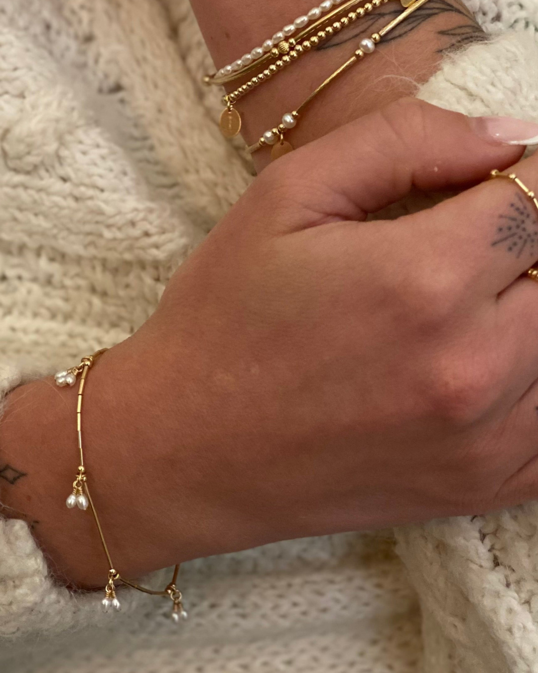 Close-up of a hand wearing multiple gold bracelets on a textured surface