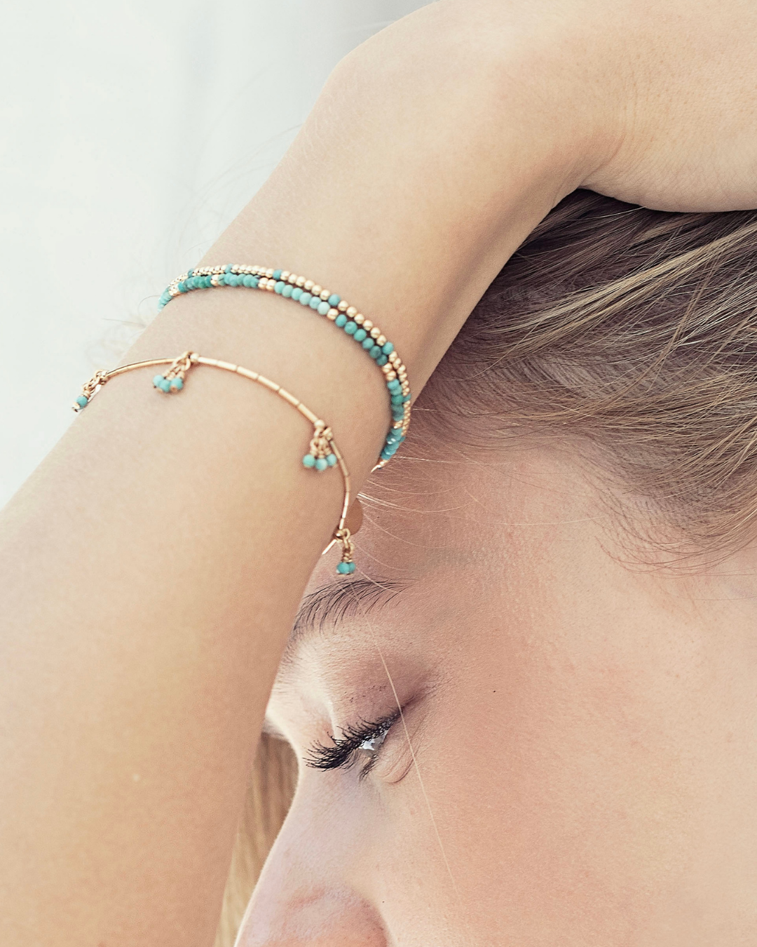 Close-up of a person wearing gold and turquoise gemstone bracelets on their wrist.