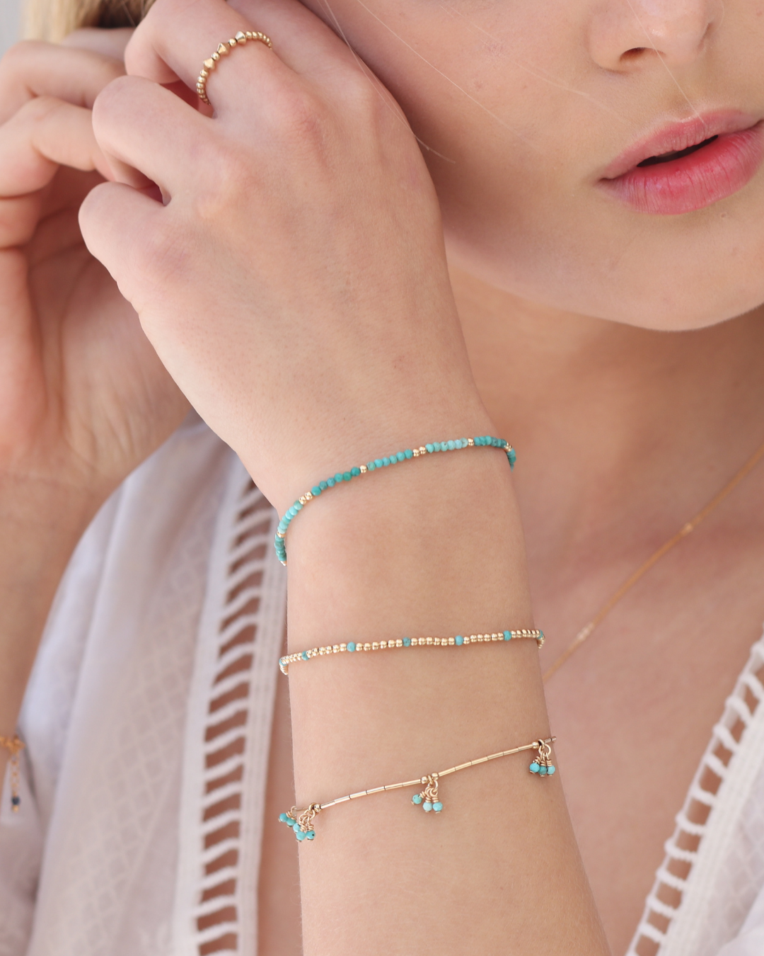 Close-up of a person wearing gold and turquoise gemstone bracelets on their wrist.
