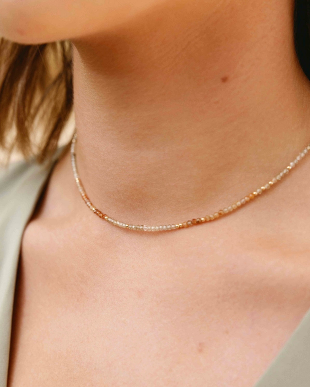 Close-up of a woman wearing a delicate  gold and zircon gemstone necklace with a neutral background