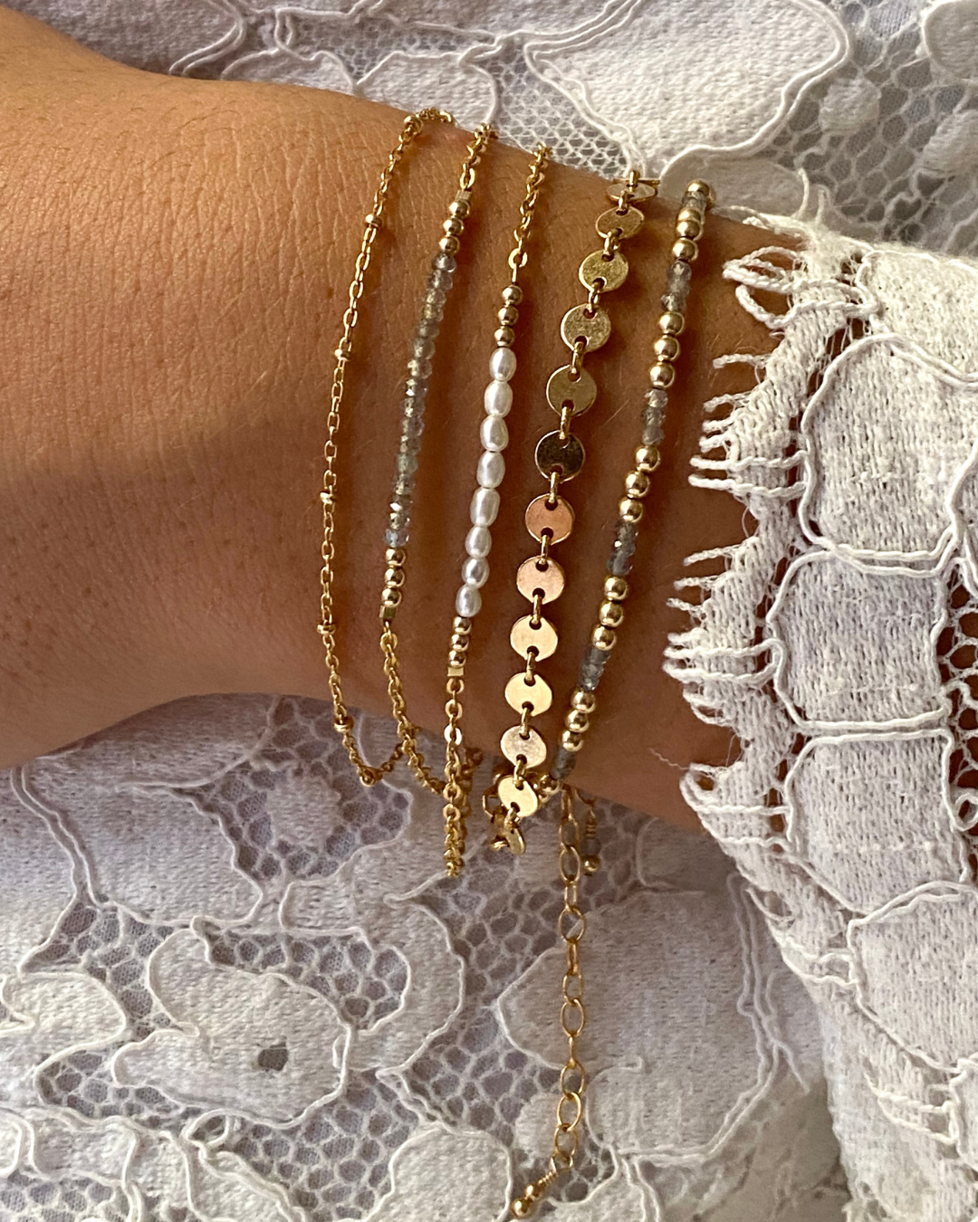Close-up of a wrist wearing multiple gold and beaded bracelets on a lace fabric background