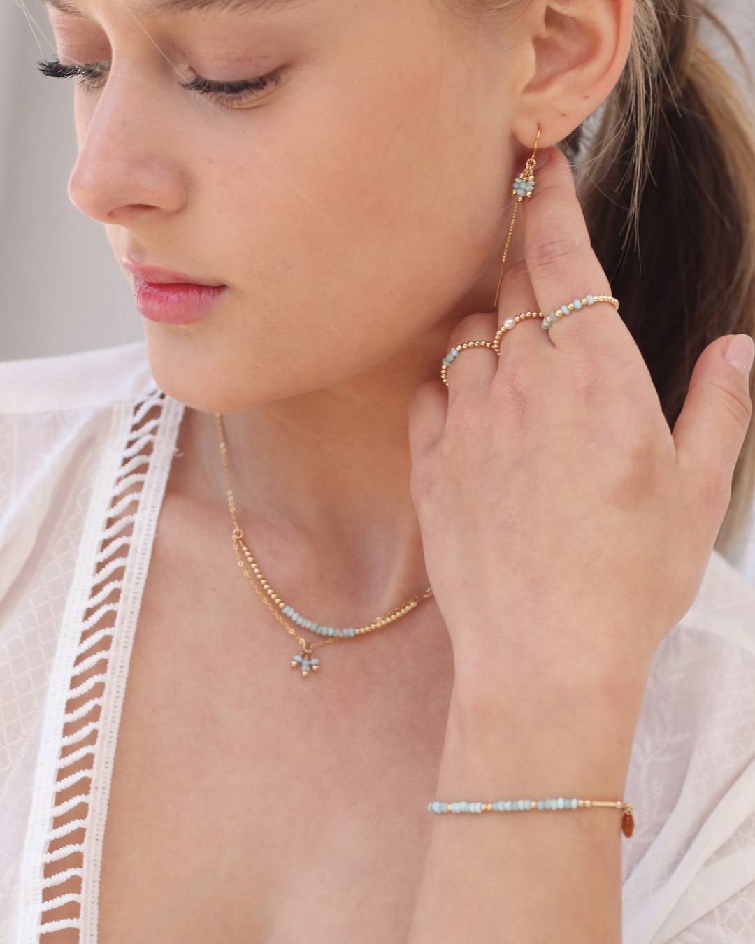 Close-up of a woman wearing gold and larimar gemstone jewellery including earrings, necklace, rings and bracelet.