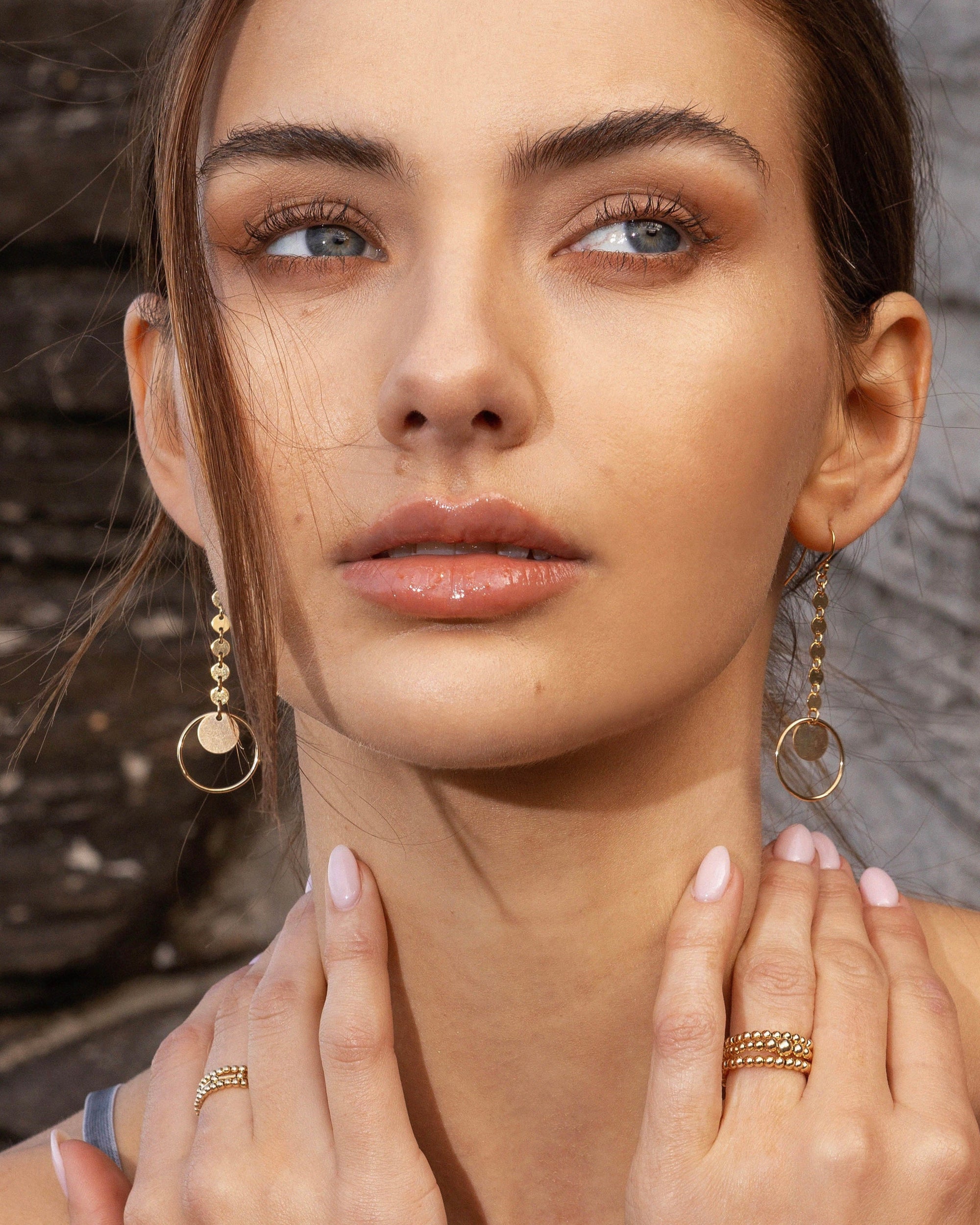 Woman wearing gold earrings and rings with a neutral background