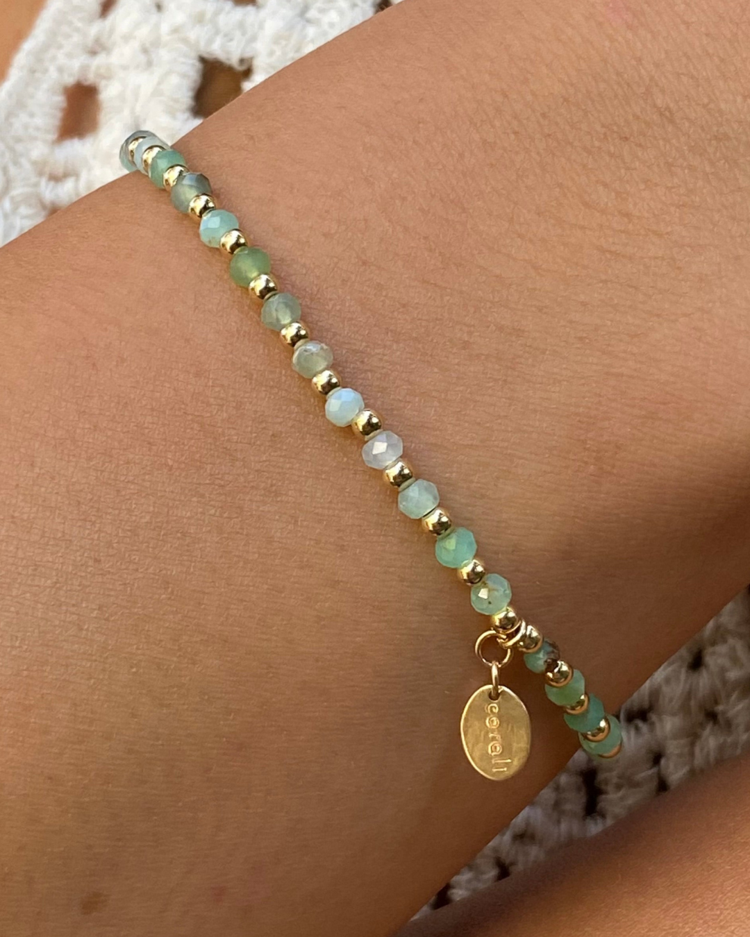 Bracelet with green beads and a gold charm on a wrist against a textured background