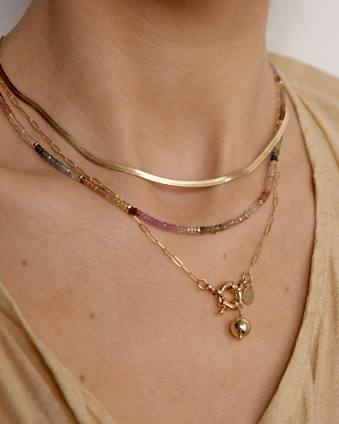 Close-up of a person wearing multiple gold necklaces with a neutral background