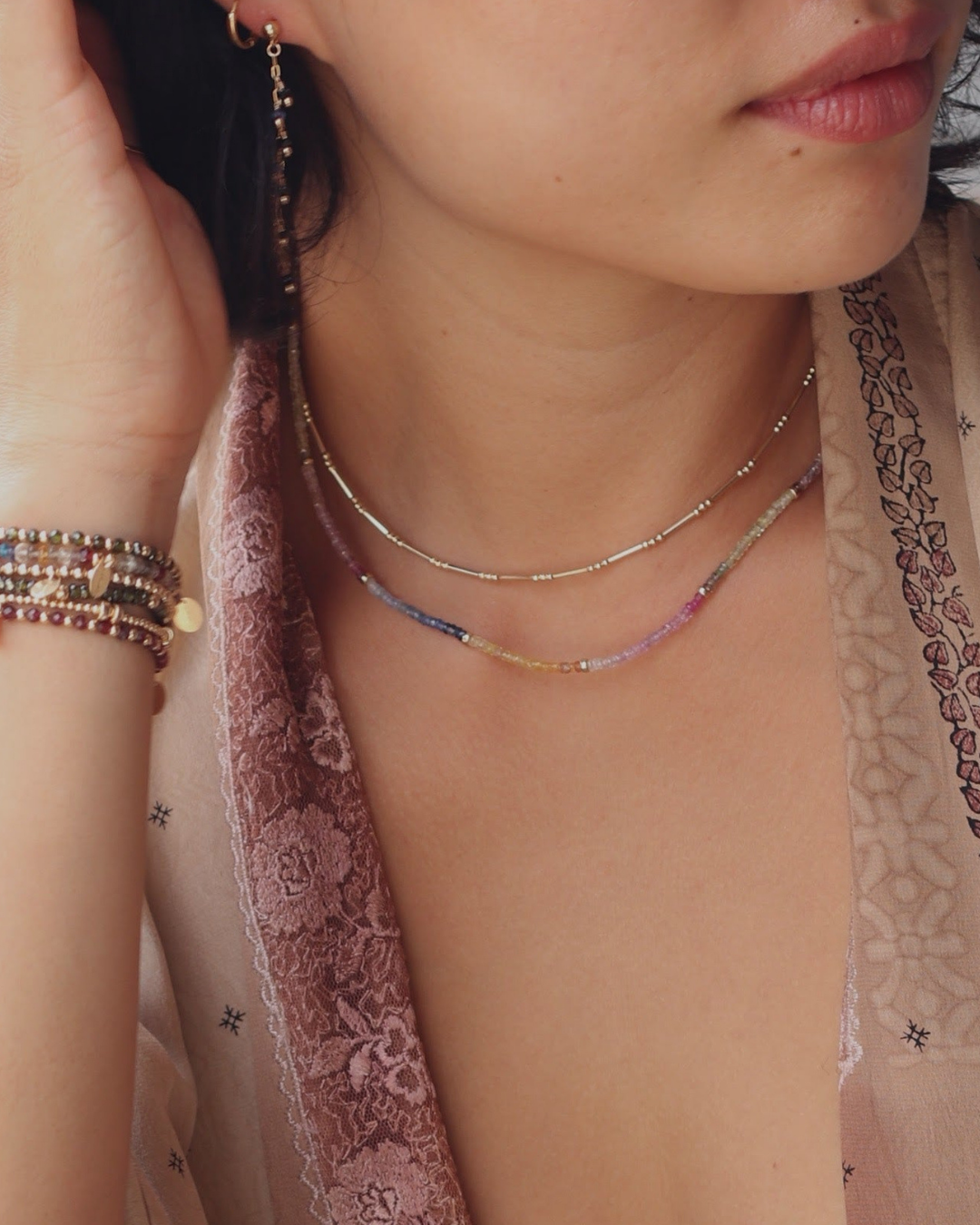 Close-up of a person wearing layered necklaces and a bracelet with a blurred background