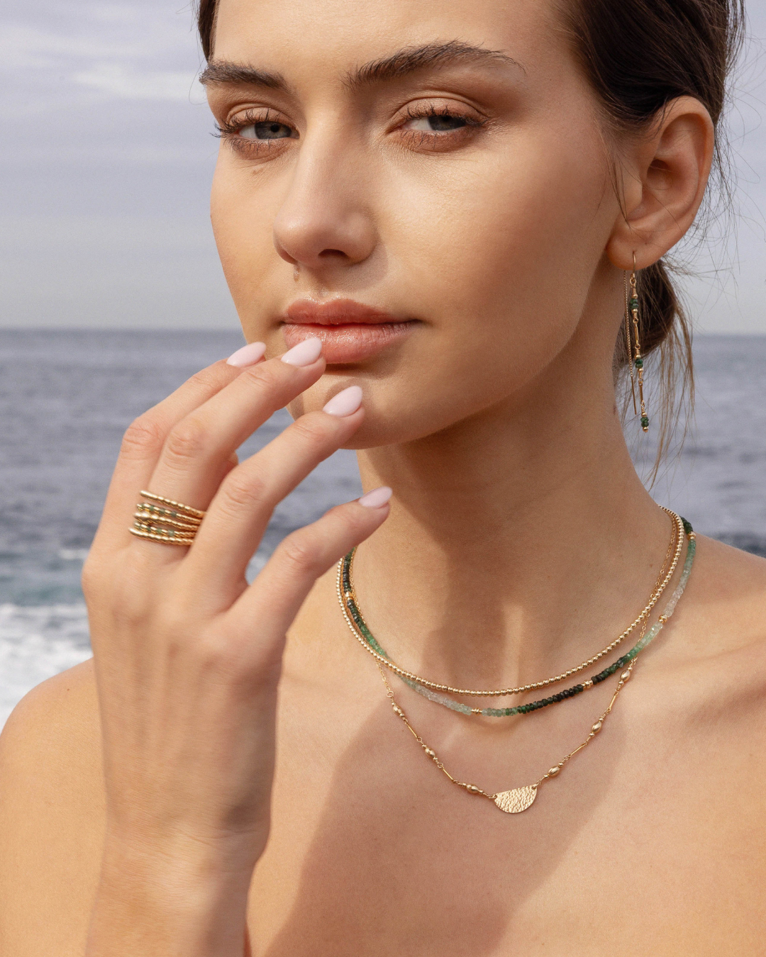 Woman wearing gold jewelry with a blurred ocean background