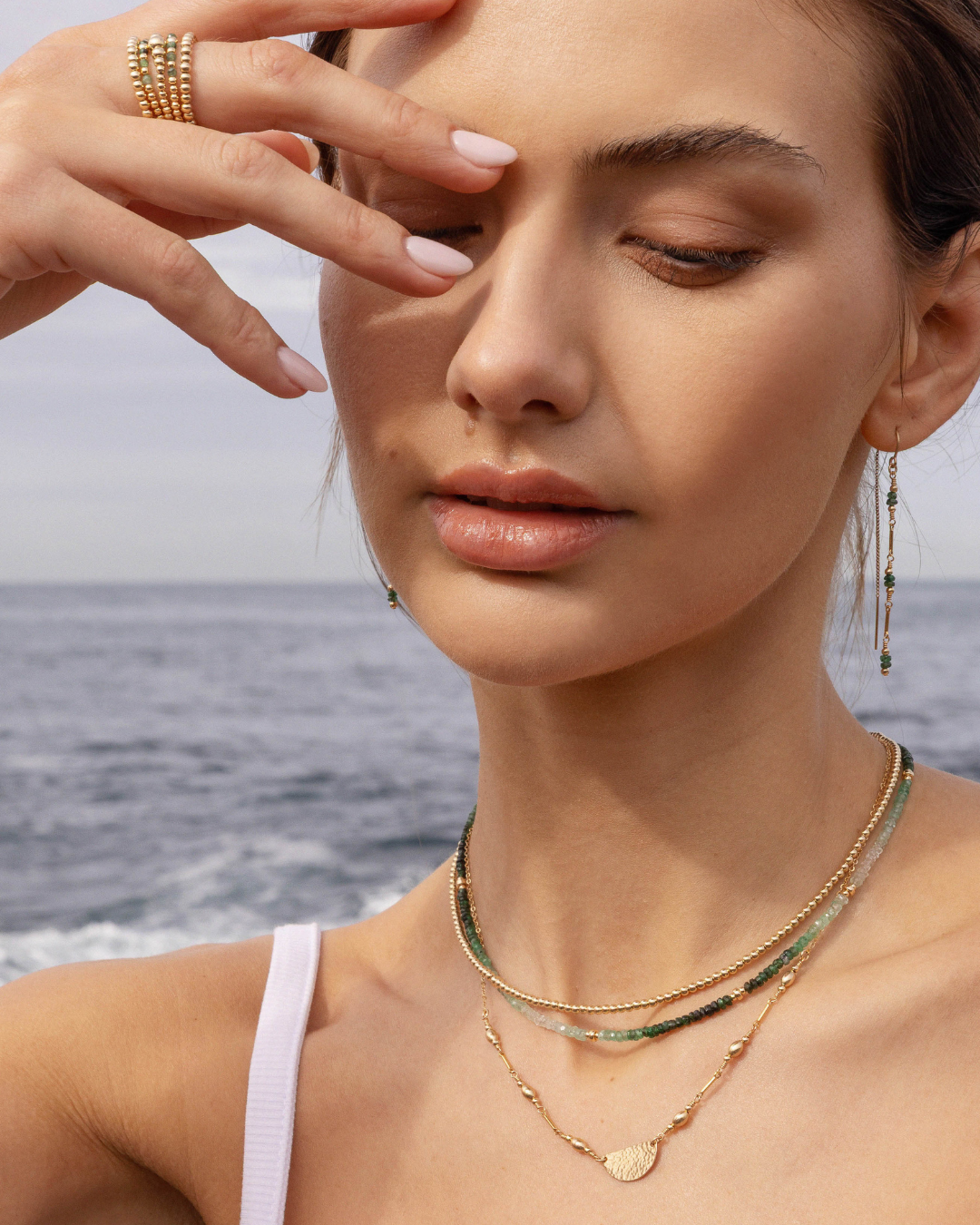 Woman wearing gold necklaces and earrings with a blurred ocean background