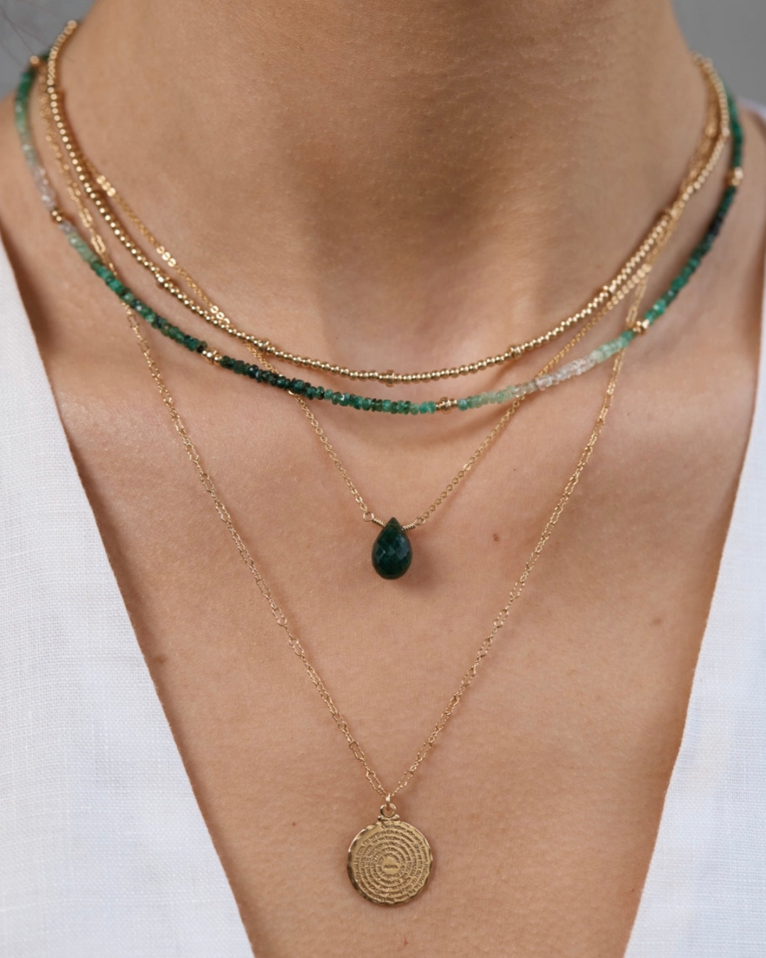 Layered gold and green necklaces on a white background