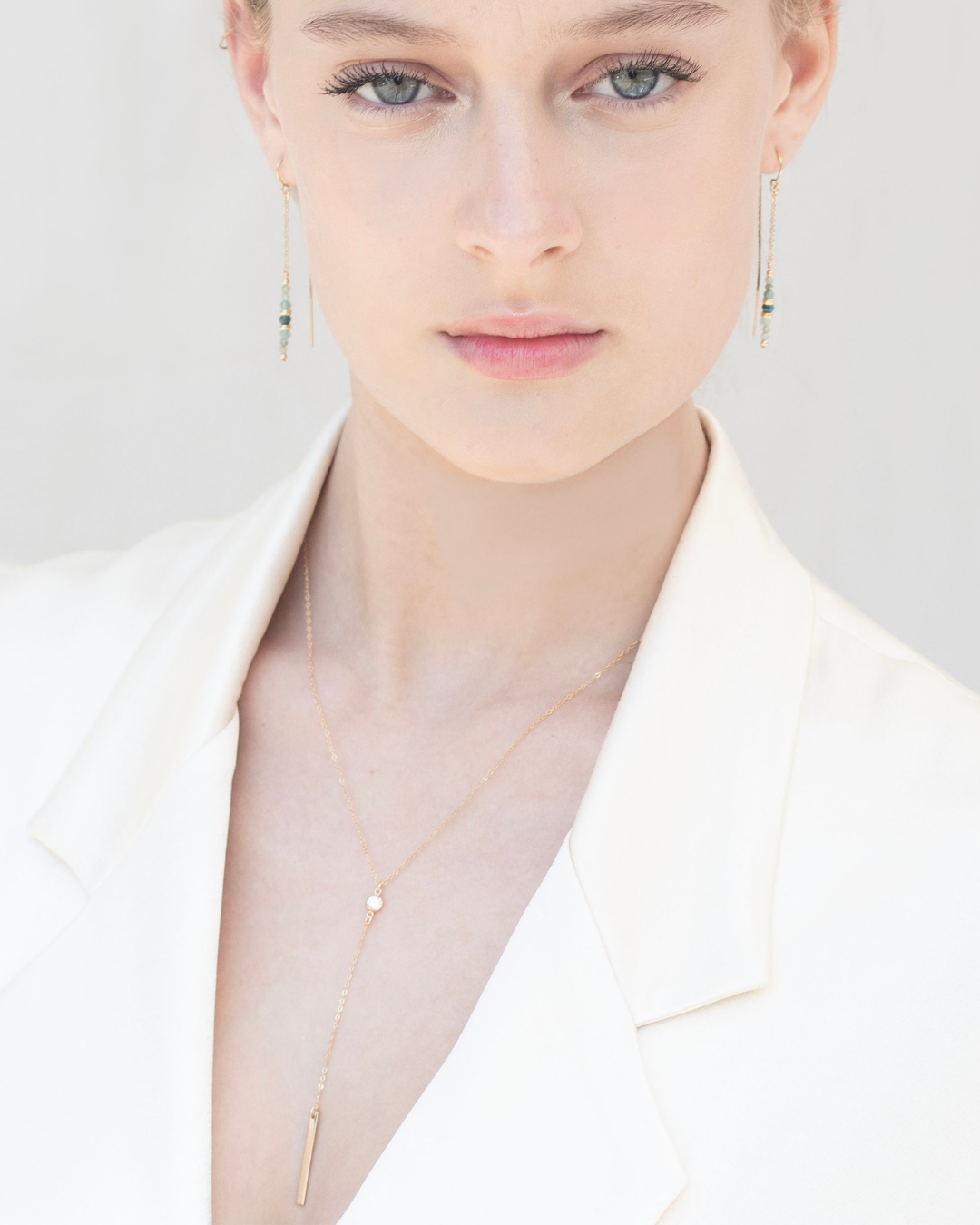 Close-up of a bride wearing a delicate gold lariat and cubic zirconia gemstone necklace and earrings on a plain background
