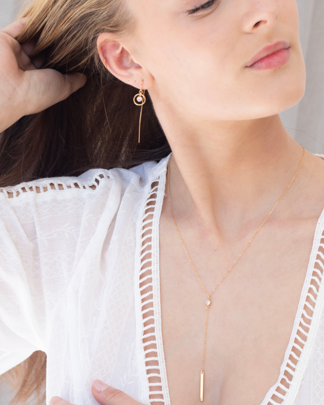 Close-up of a woman wearing gold cubic zirconia gemstone thread earrings and a lariat necklace against a neutral background