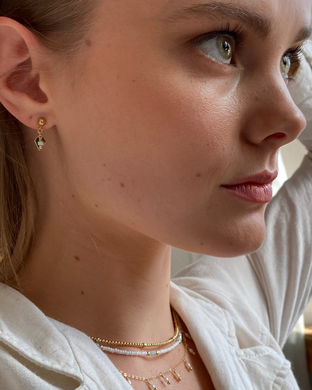 Close-up of a woman wearing gold earrings with larimar gemstone and necklaces.
