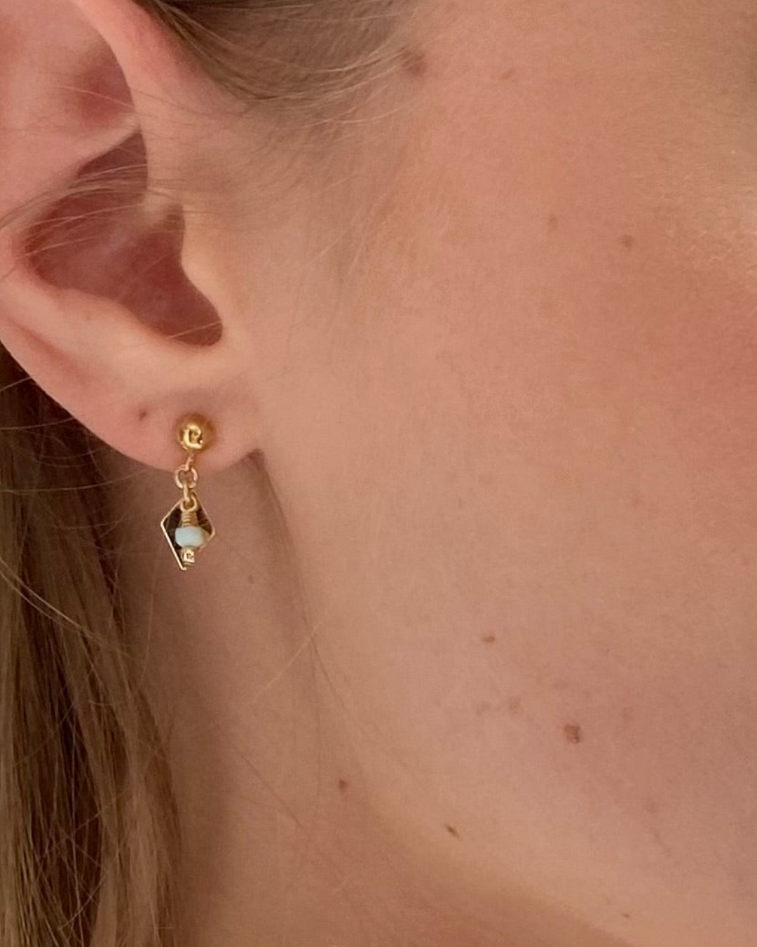 Gold earring with a small larimar gemstone worn by a person