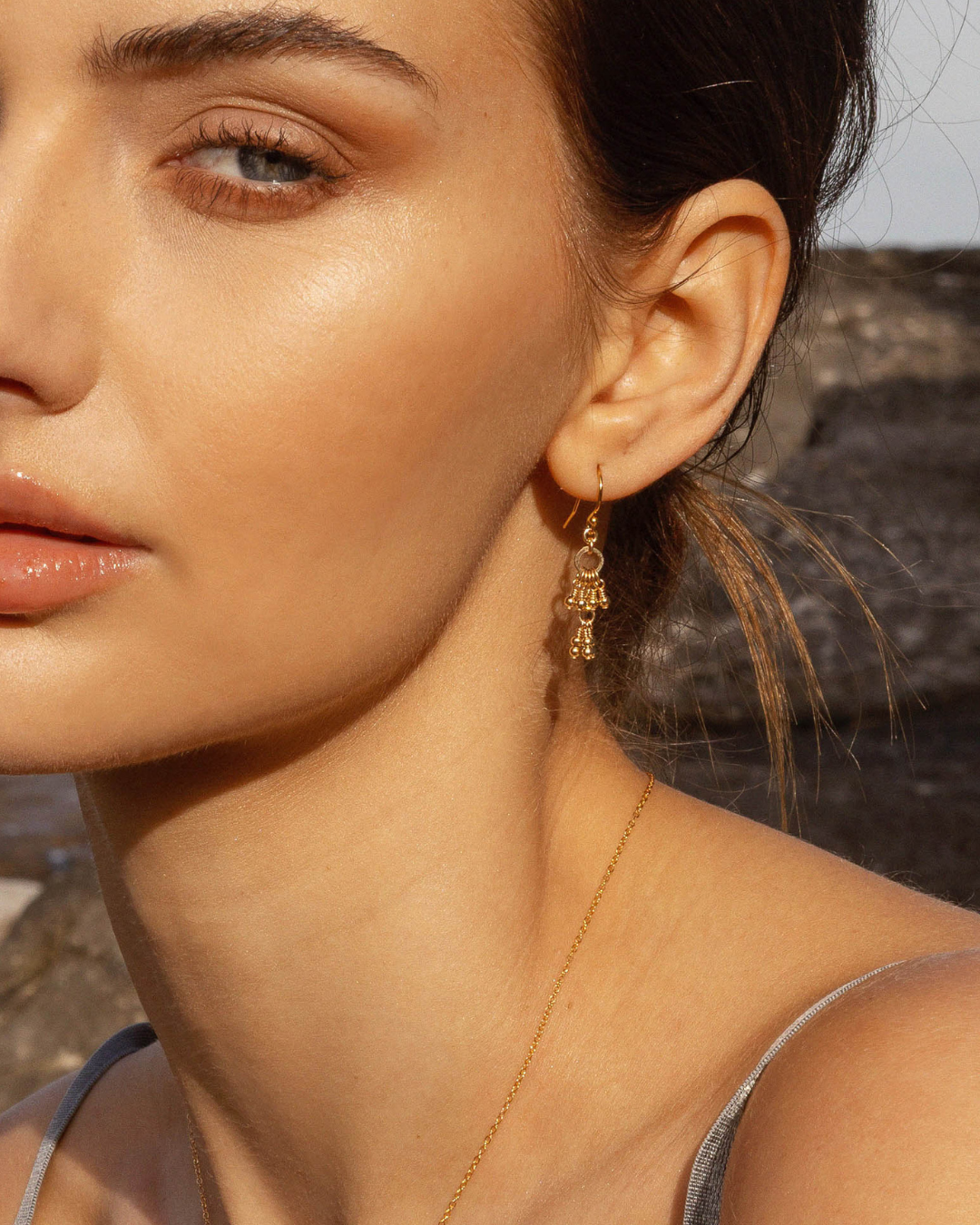 Close-up of a woman wearing gold earrings and a necklace with a blurred natural background