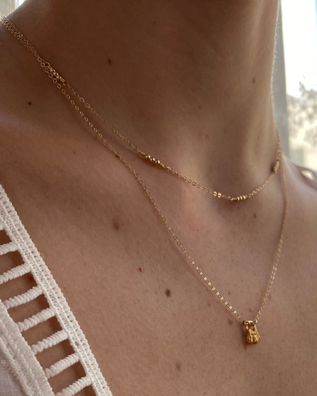 Gold necklaces with a small pendant on a person's neck