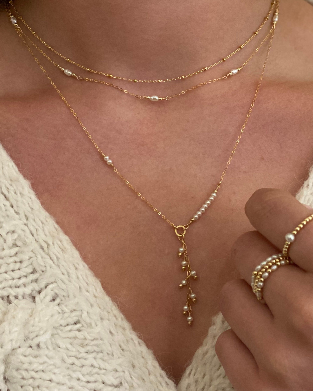 Close-up of a person wearing gold and pearl necklaces and rings.