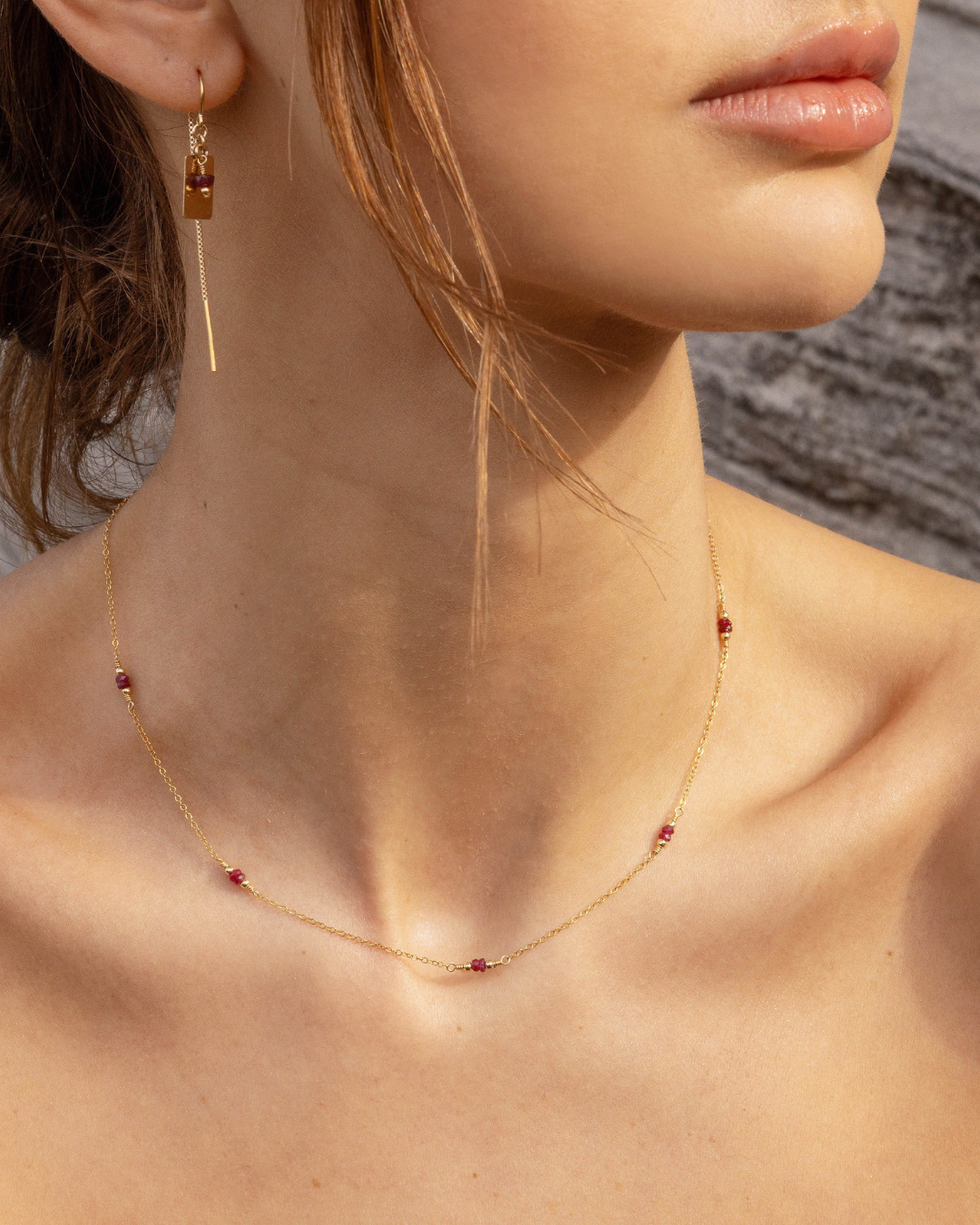 Close-up of a woman wearing a gold necklace with red ruby beads and earrings.