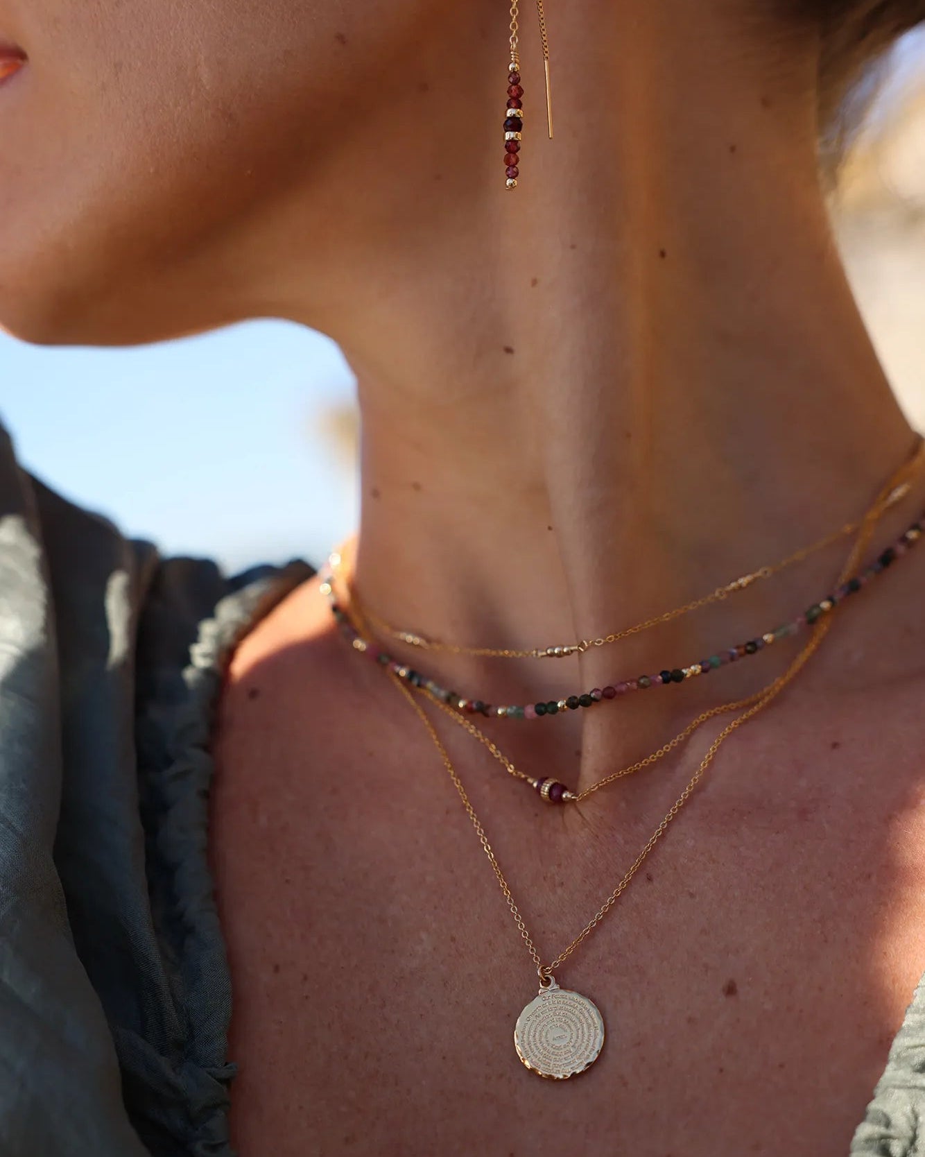 Model wearing multi coloured tourmaline gemstone and gold beaded necklace layered with other necklaces
