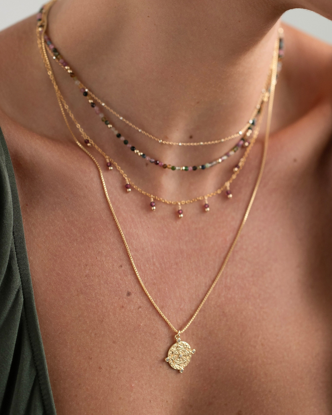 Close-up of a person wearing multiple gold necklaces with pendant.