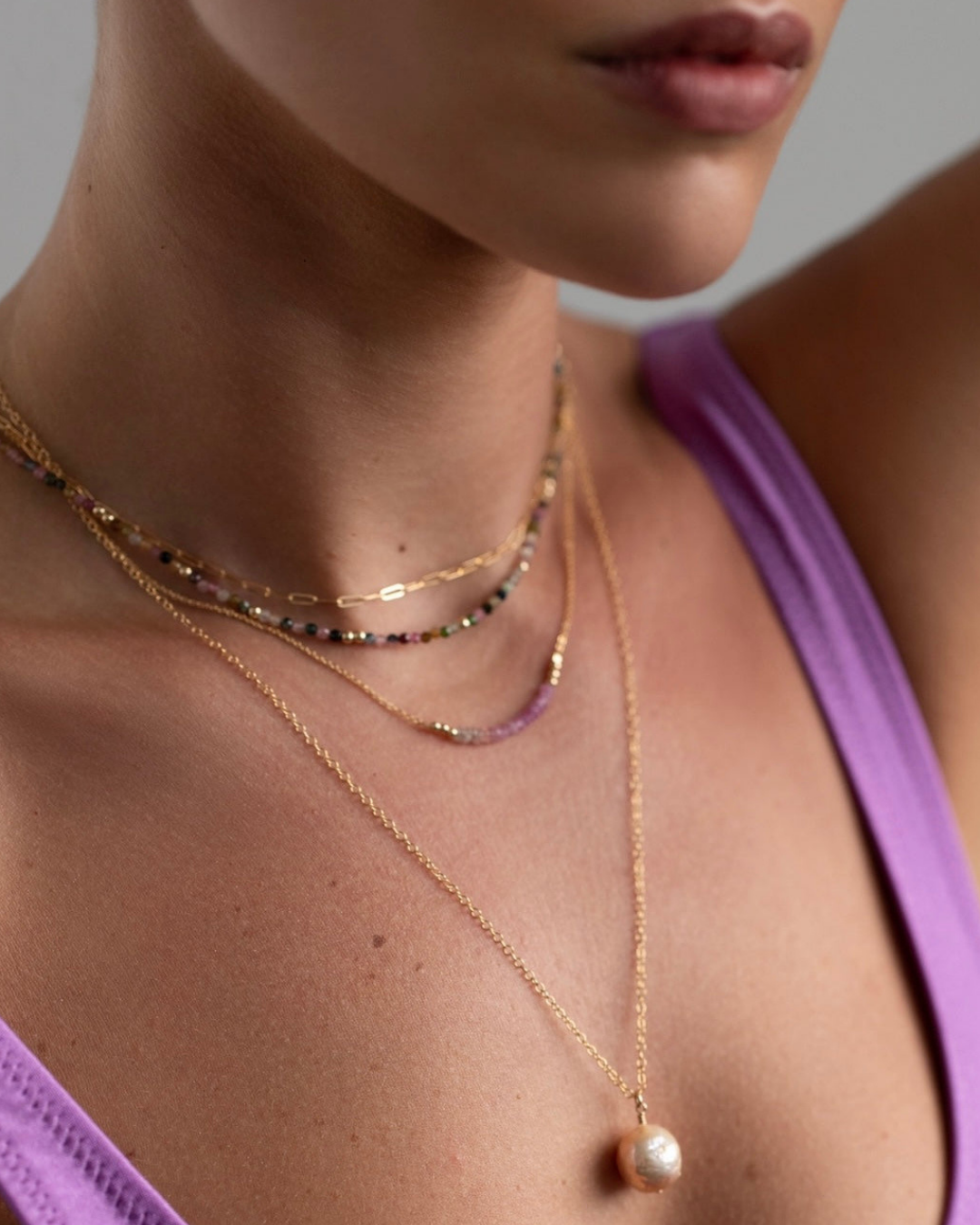 Close-up of a person wearing multiple gold necklaces with a focus on one featuring a pearl pendant.