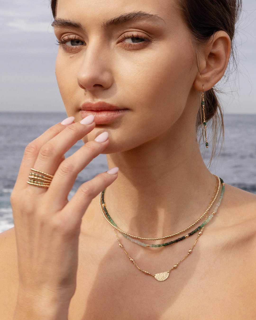 Woman wearing gold necklaces and rings with a blurred ocean background