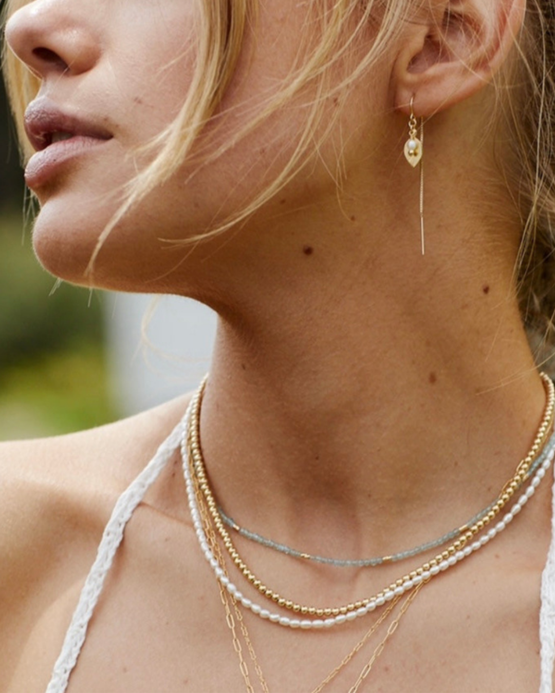 Close-up of a woman wearing gold necklaces and earrings with a blurred natural background