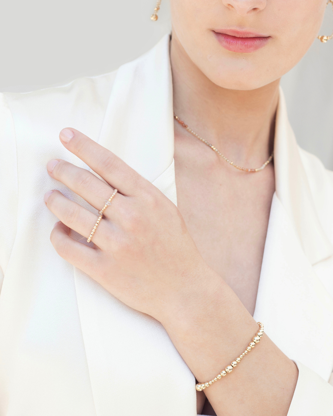 Close-up of a woman wearing gold jewellery including a rings, a bracelet, and cubic zirconia necklace on a plain background.