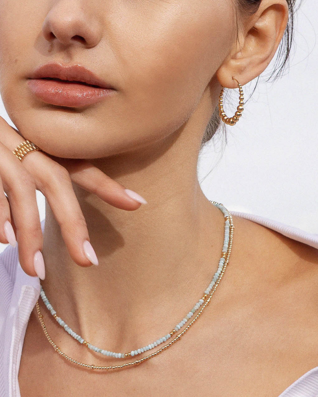 Close-up of a person wearing gold hoop earrings and a beaded necklace.