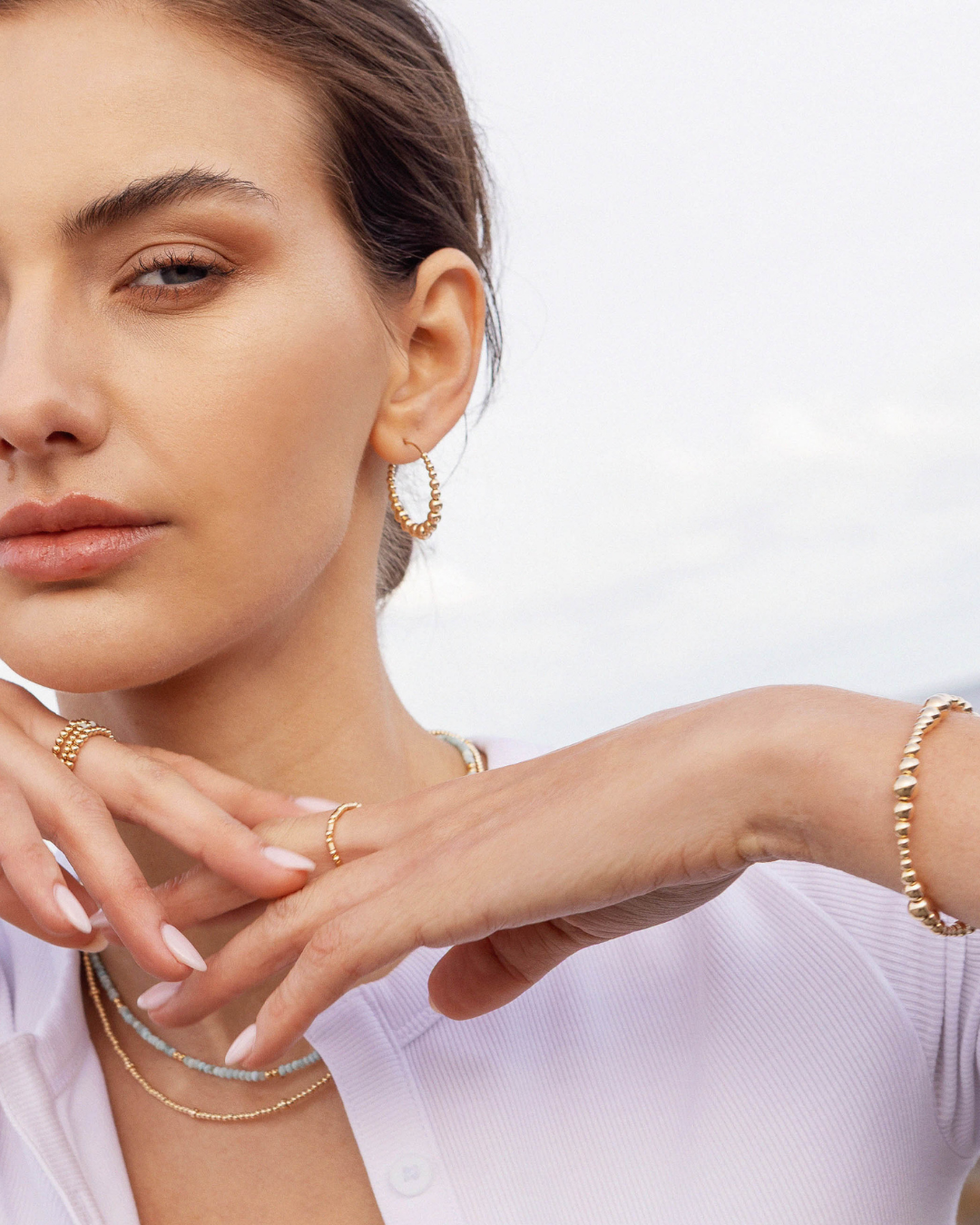 Woman wearing gold jewelry including earrings, bracelets, and rings on a white background