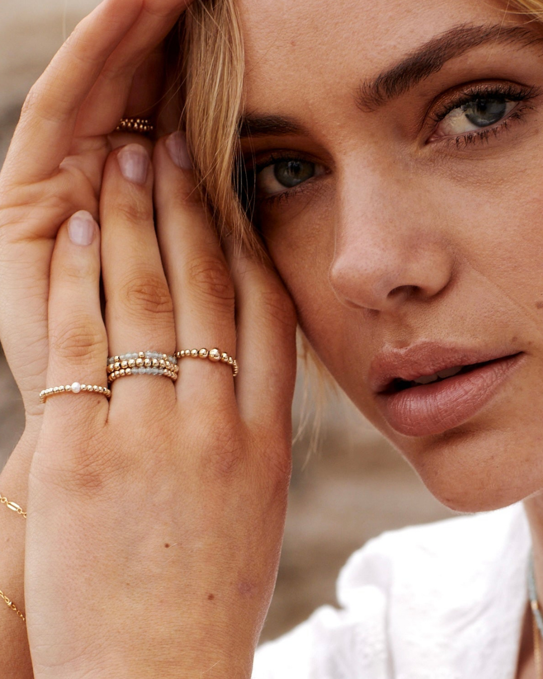 Close-up of a woman's face with gold rings on her fingers