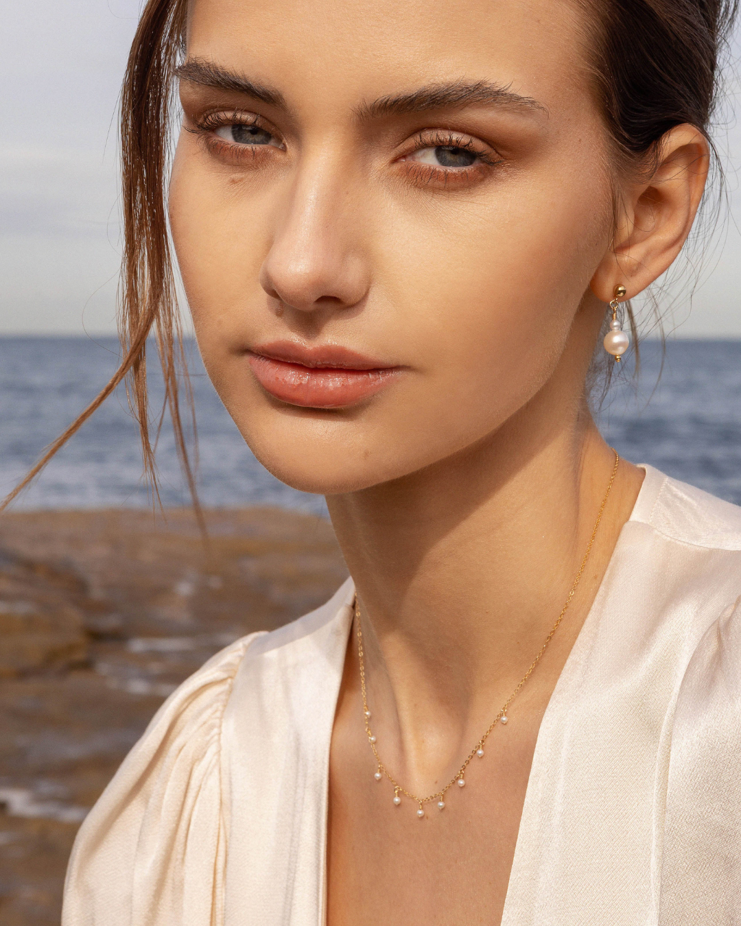 Woman with a pearl earring and necklace by the ocean