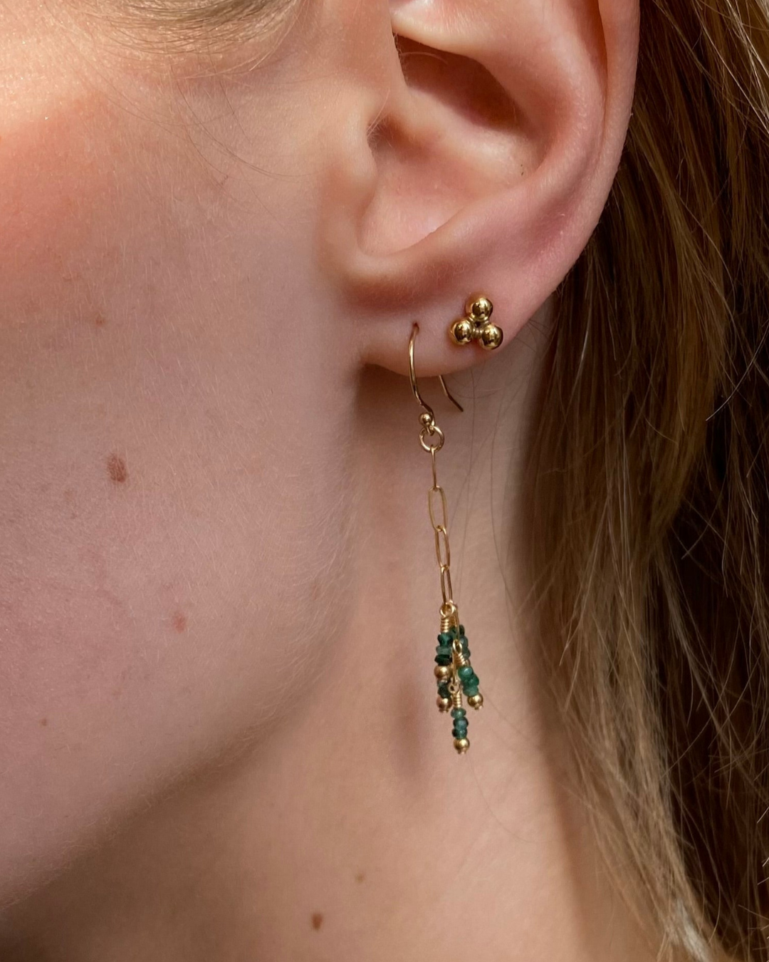 Close-up of an ear wearing gold and green earrings.