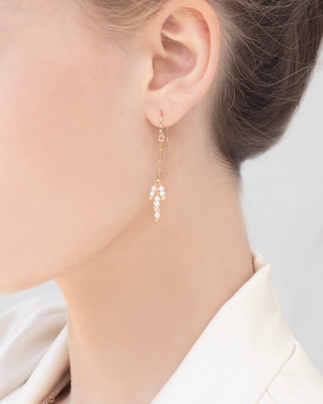 Close up of a woman wearing gold pearl earrings being worn against a neutral background