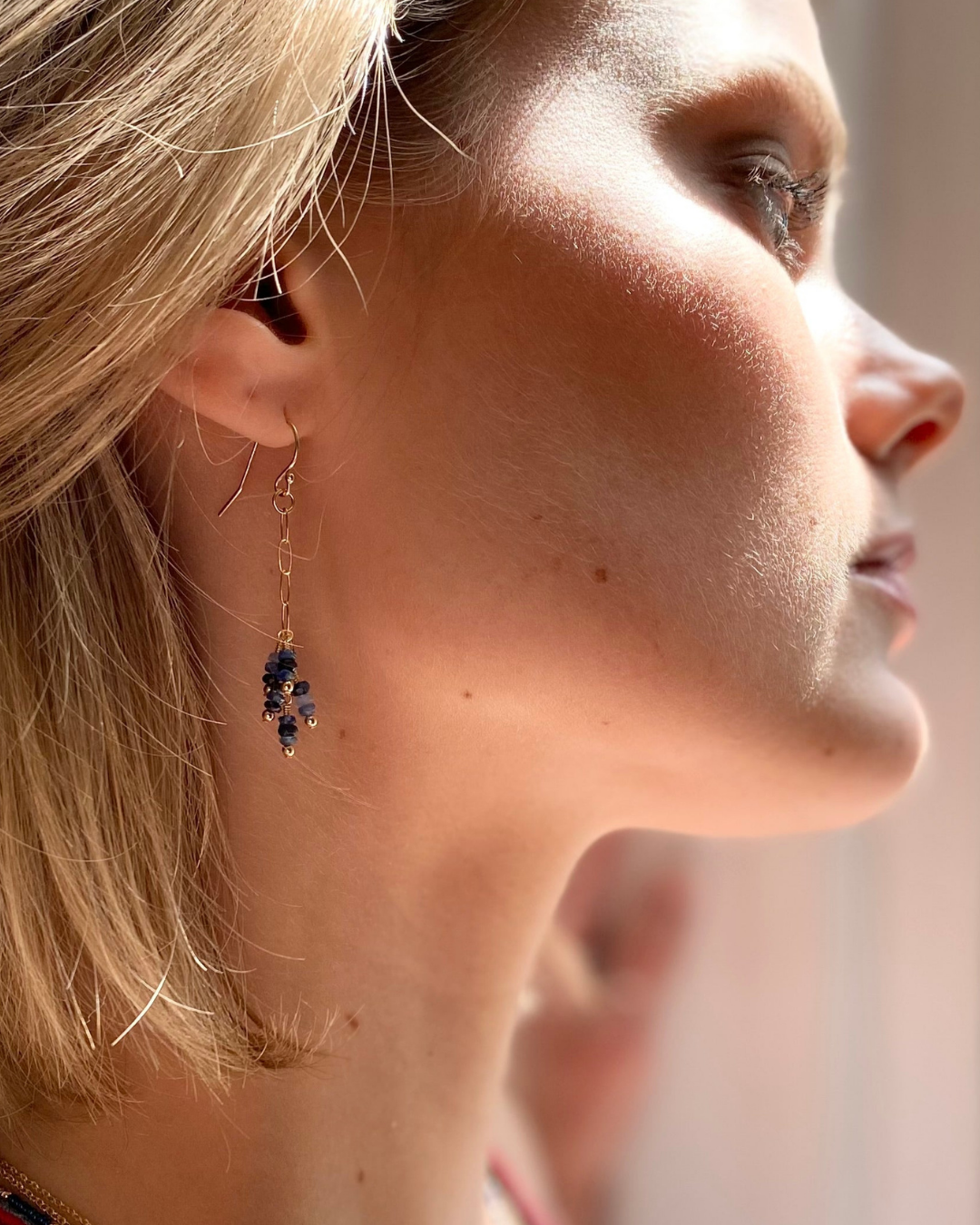 Close-up of a woman wearing a gold earring with blue sapphire stones.
